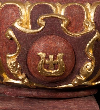 Zdjęcie nr 13: Kamienna chrzcielnica osadzona na wysokim cokole na planie kwadratu, z profilowanym, wielostopniowym trzonem, dekorowanym puklowaniem, liśćmi akantu i uskrzydlonymi główkami anielskimi. Czara puklowana, ozdobiona kartuszem z godłem herbowym Jastrzębiec od frontu oraz kartuszem z godłem herbowym Gryf po przeciwnej stronie, po bokach dwa bukraniony. Chrzcielnica polichromowana w kolorze czerwonym ze złoconymi detalami. Drewniana pokrywa w formie podstawy dekorowanej perełkowaniem i żłobkami, zwieńczona klasycystycznym wazonem zdobionym girlandami, zakończonym kwiatem. 
Chrzcielnica umieszczona w niszy drewnianej oprawy filara arkady tęczowej. Nadbudowa jest architektoniczna, dwukondygnacyjna ze zwieńczeniem. Pierwsza kondygnacja z niszą ujętą dwustrefowym cokołem, zakończonym profilowanym gzymsem dekorowanym żłobkami, zakończonym kartuszem, flankowana kwiatowymi zwisami. Druga kondygnacja z płyciną ujętą pilastrami ozdobionymi kwiatowymi zwisami, zakończonymi gzymsem przechodzącym w woluty, na których znajdują się uskrzydlone główki anielskie. W niszy na rzeźbionym fragmencie skały, flankowanym dwoma drzewami, grupa rzeźbiarska Chrztu Chrystusa. Nad nią na łuku gołębica Ducha Świętego w glorii promienistej. Zwieńczenie w kształcie zbliżonym do kwadratu, ujętego spływami wolutowymi dekorowanymi akantem, zakończone gzymsem i baldachimem. W polu, na obłoku rzeźbiona półpostać Boga Ojca z nimbem trójkątnym i promienistym wokół głowy. Baldachim na planie półkola, w formie niepełnego belkowania, na nim cztery kabłąki podtrzymujące cokół, na którym znajduje się klasycystyczny wazon. Oprawa polichromowana w kolorze seledynowym, ze złoconymi profilami i ornamentyką. 
