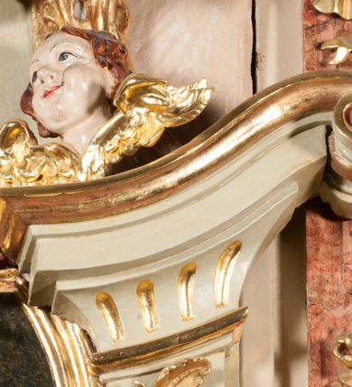 Zdjęcie nr 31: Kamienna chrzcielnica osadzona na wysokim cokole na planie kwadratu, z profilowanym, wielostopniowym trzonem, dekorowanym puklowaniem, liśćmi akantu i uskrzydlonymi główkami anielskimi. Czara puklowana, ozdobiona kartuszem z godłem herbowym Jastrzębiec od frontu oraz kartuszem z godłem herbowym Gryf po przeciwnej stronie, po bokach dwa bukraniony. Chrzcielnica polichromowana w kolorze czerwonym ze złoconymi detalami. Drewniana pokrywa w formie podstawy dekorowanej perełkowaniem i żłobkami, zwieńczona klasycystycznym wazonem zdobionym girlandami, zakończonym kwiatem. 
Chrzcielnica umieszczona w niszy drewnianej oprawy filara arkady tęczowej. Nadbudowa jest architektoniczna, dwukondygnacyjna ze zwieńczeniem. Pierwsza kondygnacja z niszą ujętą dwustrefowym cokołem, zakończonym profilowanym gzymsem dekorowanym żłobkami, zakończonym kartuszem, flankowana kwiatowymi zwisami. Druga kondygnacja z płyciną ujętą pilastrami ozdobionymi kwiatowymi zwisami, zakończonymi gzymsem przechodzącym w woluty, na których znajdują się uskrzydlone główki anielskie. W niszy na rzeźbionym fragmencie skały, flankowanym dwoma drzewami, grupa rzeźbiarska Chrztu Chrystusa. Nad nią na łuku gołębica Ducha Świętego w glorii promienistej. Zwieńczenie w kształcie zbliżonym do kwadratu, ujętego spływami wolutowymi dekorowanymi akantem, zakończone gzymsem i baldachimem. W polu, na obłoku rzeźbiona półpostać Boga Ojca z nimbem trójkątnym i promienistym wokół głowy. Baldachim na planie półkola, w formie niepełnego belkowania, na nim cztery kabłąki podtrzymujące cokół, na którym znajduje się klasycystyczny wazon. Oprawa polichromowana w kolorze seledynowym, ze złoconymi profilami i ornamentyką. 
