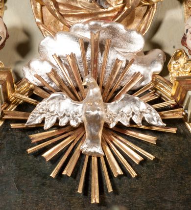 Zdjęcie nr 30: Kamienna chrzcielnica osadzona na wysokim cokole na planie kwadratu, z profilowanym, wielostopniowym trzonem, dekorowanym puklowaniem, liśćmi akantu i uskrzydlonymi główkami anielskimi. Czara puklowana, ozdobiona kartuszem z godłem herbowym Jastrzębiec od frontu oraz kartuszem z godłem herbowym Gryf po przeciwnej stronie, po bokach dwa bukraniony. Chrzcielnica polichromowana w kolorze czerwonym ze złoconymi detalami. Drewniana pokrywa w formie podstawy dekorowanej perełkowaniem i żłobkami, zwieńczona klasycystycznym wazonem zdobionym girlandami, zakończonym kwiatem. 
Chrzcielnica umieszczona w niszy drewnianej oprawy filara arkady tęczowej. Nadbudowa jest architektoniczna, dwukondygnacyjna ze zwieńczeniem. Pierwsza kondygnacja z niszą ujętą dwustrefowym cokołem, zakończonym profilowanym gzymsem dekorowanym żłobkami, zakończonym kartuszem, flankowana kwiatowymi zwisami. Druga kondygnacja z płyciną ujętą pilastrami ozdobionymi kwiatowymi zwisami, zakończonymi gzymsem przechodzącym w woluty, na których znajdują się uskrzydlone główki anielskie. W niszy na rzeźbionym fragmencie skały, flankowanym dwoma drzewami, grupa rzeźbiarska Chrztu Chrystusa. Nad nią na łuku gołębica Ducha Świętego w glorii promienistej. Zwieńczenie w kształcie zbliżonym do kwadratu, ujętego spływami wolutowymi dekorowanymi akantem, zakończone gzymsem i baldachimem. W polu, na obłoku rzeźbiona półpostać Boga Ojca z nimbem trójkątnym i promienistym wokół głowy. Baldachim na planie półkola, w formie niepełnego belkowania, na nim cztery kabłąki podtrzymujące cokół, na którym znajduje się klasycystyczny wazon. Oprawa polichromowana w kolorze seledynowym, ze złoconymi profilami i ornamentyką. 
