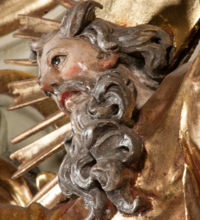 Zdjęcie nr 38: Kamienna chrzcielnica osadzona na wysokim cokole na planie kwadratu, z profilowanym, wielostopniowym trzonem, dekorowanym puklowaniem, liśćmi akantu i uskrzydlonymi główkami anielskimi. Czara puklowana, ozdobiona kartuszem z godłem herbowym Jastrzębiec od frontu oraz kartuszem z godłem herbowym Gryf po przeciwnej stronie, po bokach dwa bukraniony. Chrzcielnica polichromowana w kolorze czerwonym ze złoconymi detalami. Drewniana pokrywa w formie podstawy dekorowanej perełkowaniem i żłobkami, zwieńczona klasycystycznym wazonem zdobionym girlandami, zakończonym kwiatem. 
Chrzcielnica umieszczona w niszy drewnianej oprawy filara arkady tęczowej. Nadbudowa jest architektoniczna, dwukondygnacyjna ze zwieńczeniem. Pierwsza kondygnacja z niszą ujętą dwustrefowym cokołem, zakończonym profilowanym gzymsem dekorowanym żłobkami, zakończonym kartuszem, flankowana kwiatowymi zwisami. Druga kondygnacja z płyciną ujętą pilastrami ozdobionymi kwiatowymi zwisami, zakończonymi gzymsem przechodzącym w woluty, na których znajdują się uskrzydlone główki anielskie. W niszy na rzeźbionym fragmencie skały, flankowanym dwoma drzewami, grupa rzeźbiarska Chrztu Chrystusa. Nad nią na łuku gołębica Ducha Świętego w glorii promienistej. Zwieńczenie w kształcie zbliżonym do kwadratu, ujętego spływami wolutowymi dekorowanymi akantem, zakończone gzymsem i baldachimem. W polu, na obłoku rzeźbiona półpostać Boga Ojca z nimbem trójkątnym i promienistym wokół głowy. Baldachim na planie półkola, w formie niepełnego belkowania, na nim cztery kabłąki podtrzymujące cokół, na którym znajduje się klasycystyczny wazon. Oprawa polichromowana w kolorze seledynowym, ze złoconymi profilami i ornamentyką. 
