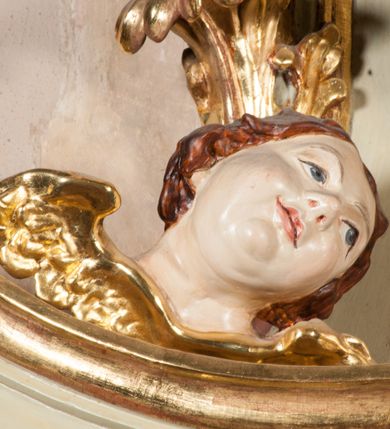 Zdjęcie nr 34: Kamienna chrzcielnica osadzona na wysokim cokole na planie kwadratu, z profilowanym, wielostopniowym trzonem, dekorowanym puklowaniem, liśćmi akantu i uskrzydlonymi główkami anielskimi. Czara puklowana, ozdobiona kartuszem z godłem herbowym Jastrzębiec od frontu oraz kartuszem z godłem herbowym Gryf po przeciwnej stronie, po bokach dwa bukraniony. Chrzcielnica polichromowana w kolorze czerwonym ze złoconymi detalami. Drewniana pokrywa w formie podstawy dekorowanej perełkowaniem i żłobkami, zwieńczona klasycystycznym wazonem zdobionym girlandami, zakończonym kwiatem. 
Chrzcielnica umieszczona w niszy drewnianej oprawy filara arkady tęczowej. Nadbudowa jest architektoniczna, dwukondygnacyjna ze zwieńczeniem. Pierwsza kondygnacja z niszą ujętą dwustrefowym cokołem, zakończonym profilowanym gzymsem dekorowanym żłobkami, zakończonym kartuszem, flankowana kwiatowymi zwisami. Druga kondygnacja z płyciną ujętą pilastrami ozdobionymi kwiatowymi zwisami, zakończonymi gzymsem przechodzącym w woluty, na których znajdują się uskrzydlone główki anielskie. W niszy na rzeźbionym fragmencie skały, flankowanym dwoma drzewami, grupa rzeźbiarska Chrztu Chrystusa. Nad nią na łuku gołębica Ducha Świętego w glorii promienistej. Zwieńczenie w kształcie zbliżonym do kwadratu, ujętego spływami wolutowymi dekorowanymi akantem, zakończone gzymsem i baldachimem. W polu, na obłoku rzeźbiona półpostać Boga Ojca z nimbem trójkątnym i promienistym wokół głowy. Baldachim na planie półkola, w formie niepełnego belkowania, na nim cztery kabłąki podtrzymujące cokół, na którym znajduje się klasycystyczny wazon. Oprawa polichromowana w kolorze seledynowym, ze złoconymi profilami i ornamentyką. 
