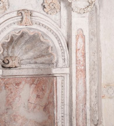 Zdjęcie nr 8: Kamienny lawetarz został osadzony na cokole, którego front zdobi putto trzymające w ręce kartusz herbowy z nieczytelnym godłem. Pod kartuszem widoczna jest czworoboczna wnęka. Nad cokołem znajduje się nisza konchowa z konchą wypełnioną muszlą, ujęta jońskimi pilastrami podtrzymującymi belkowanie, którego fryz ozdobiono główkami aniołków. Archiwolta ponad konchą została na środku przewiązana wolutowym kluczem. Z kolei w przyłuczu konchy znalazły się dwie rozety. Kapitele pilastrów flankujące niszę dodatkowo dekorowane są podwieszonymi girlandami, zaś ich trzony wydłużonymi płycinami. Architraw i gzyms zdobione są kostkowaniem. Na belkowaniu widnieje inskrypcja: „T(HOMAS) O(LINSKI) P(LEBANUS) N(IEPOLOMICENSIS) / A(NNO) D(OMINI) 1696”. Całość wieńczy figura diakona ubranego w białą albę i pomarańczową dalmatykę. W lewej ręce trzyma zamkniętą księgę. Prawa ręka uniesiona na wysokości pasa jest uszkodzona.