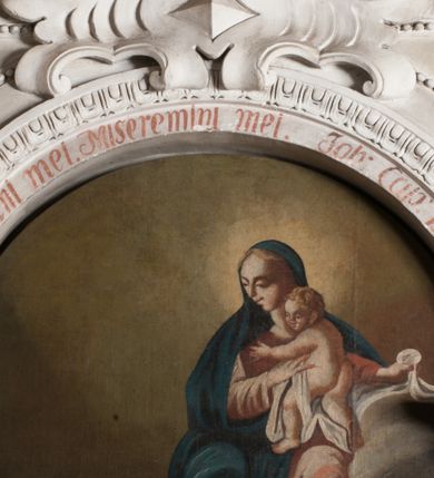 Zdjęcie nr 3: Obraz ma kształt stojacego prostokąta zamkniętego łukiem pełnym. Na tle szarożółtych obłoków ukazano w całej postaci św. Karola Boromeusza klęczącego przed siedzącą na obłokach Madonną z Dzieciątkiem. Święty został ukazany w trzech czwartych zwrócony w lewo ze złożonymi rękami do modlitwy. Przedstawiono go z uniesioną głową zwróconą w stronę Matki Boskiej. Jego twarz o różowo-szarawej karnacji charakteryzuje się wydatnym nosem i ustami oraz ciemnymi oczami. Na jego głowie widoczna jest tonsura, wycięta w ciemnobrązowych włosach. Święty ubrany jest w strój kardynalski, purpurową sutannę i mucet oraz w białą komżę zdobioną u spodu haftem. Ukazana z lewej strony Madonna z Dzieciątkiem zwrócona jest w trzech czwartych w prawo. Maria podtrzymuje małego Jezusa stojącego na jej lewym kolanie, który w jej stronę wyciąga obie rączki. Twarz Madonny ma nieznacznie zniekształcone rysy. Ma jasną karnację, prosty nos, wąskie, lekko uśmiechnięte usta i półprzymknięte oczy. Jej głowę otaczają blond włosy rozdzielone pośrodku przedziałkiem. Maria ubrana jest w bladoróżową suknię z długimi rękawami oraz ciemnoniebieski maforion spływający z głowy, okrywający jej ramiona oraz prawą nogę. Trzymane przez nią Dzieciątko jest nagie. Tylko nieznacznie lewą nóżkę zakrywa biała chusta, której koniec Madonna trzyma w lekko uniesionej lewej ręce. Mały Jezus jest zwrócony w trzech czwartych w prawo. Ma okrągłą twarz z małym szerokim nosem, ciemnymi oczami i lekko uśmiechniętymi ustami. Jego głowę okalają jasne włosy układające się w lekko skręcone pukle. Poniżej Madonny z Dzieciątkiem w rogu obrazu widoczne są dusze w ogniu czyścowym. Są to dwie postacie wyłaniające się w popiersiach z ognistych płomieni z głowami zwróconymi w stronę Maryi i Jezusa. Jedna z nich ma uniesioną w geście wołania o pomoc prawą rękę. Ponad obrazem na archiwolcie arkady widnieje czerwony łaciński napis: Misereremini mei. Misereremini mei. Joa[nnes]. Cap[ut]. 19. vers[us] 21. Z kolei na dolnej krawędzi arkady znajduje się czerwony napis polski: Nad umarłemi Karol miał politowanie. / Bo i skarby rozdawał i modlił się za nie.