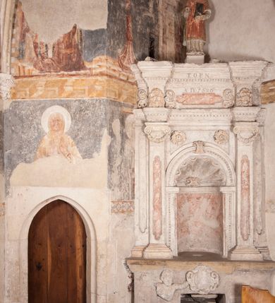 Zdjęcie nr 3: Zachowana dekoracja malarska znajduje się w tzw. starej zakrystii, określanej także jako oratorium królewskie. Dobudowano ją od północy do prezbiterium niepołomickiego kościoła. Jest to niewielka budowla na rzucie wydłużonego prostokąta, nakryta trójprzęsłowym krzyżowo-żebrowym sklepieniem, od wschodu zamknięta dwubocznie. Od zachodu w narożniku południowym widoczne jest załamanie muru, tworzącego dwie ściany wieżyczki schodowej. Do jej wnętrza prowadzi ostrołukowy portal. Oratorium oświetlają trzy ostrołukowe okna. Tylko czwarte, obecnie zamurowane, przeprute w murze północno-wschodnim pochodzi z czasów budowy kościoła. Stara zakrystia połączona jest z kościołem za pomocą ostrołukowego, profilowanego kamiennego portalu umieszczonego w środkowym przęśle ściany południowej. Na sklepieniu znajdują się rzeźbione zworniki z przedstawieniem w przęśle wschodnim głowy Chrystusa w nimbie krzyżowym, w środkowym maski liściastej, a w zachodnim motywów roślinnych. Podobnie rzeźbione motywy roślinne  pokrywają wsporniki, na które spływają żebra. 
Zachowana polichromia tworzy z architekturą starej zakrystii harmonijną całość. Białe wysklepki sklepień otoczone są wielobarwnymi, namalowanymi wzdłuż żeber, iluzjonistyczno-geometrycznymi pasami imitującymi kamienne inkrustacje w typie &quot;arte cosmatesca&quot;. Pierwotnie polichromowane były także same żebra oraz rzeźbione zworniki i wsporniki. Pionowym rytmom barwnych pasów przeciwstawiają się na ścianie wschodniej, południowej i zachodniej dwa poziome, iluzjonistyczne malowane fryzy. Górny, w odcieniach brązów jest szerszy i przypomina gzyms. Przebiega w połowie wysokości ścian, na poziomie wsporników. Poniżej znajduje się drugi, o połowę węższy, skomponowany z wielobarwnych geometrycznych rozet w rombowych polach. Fryzy wyznaczają trzy strefy dekoracji. Dolny pas uległ zniszczeniu za wyjątkiem niewielkiego fragmentu iluzjonistycznie malowanej konsolki na ścianie południowej. Dla strefy środkowej głównej tło stanowi niebieska barwa. Niestety oba te pasy obecnie są mocno uszkodzone. 
Pierwotnie pas środkowy ścian zajmowały naturalnej wielkości postacie kobiece, ujęte powyżej kolan. Z namalowanych dwunastu świętych do naszych czasów przetrwało sześć - w całości cztery (na ścianie wschodniej, południowej i zachodniej) oraz jedna bez głowy (ściana południowa) i jedna w połowie (ściana zachodnia). Są to jasno lub ciemnowłose młode kobiety, trzymające palmy męczeństwa. Ubrane są w suknie z narzuconymi płaszczami w kolorach żółtym, oliwkowym, różowym, liliowym, brązowym i błękitnym. Jedna z nich, wyobrażona ponad wejściem na klatkę schodową w wieżyczce, jest ukazana jako kobieta w podeszłym wieku z okrytą głową i dłońmi uniesionymi na wysokość piersi w geście orantki. Głowy męczennic i orantki okalają plastycznie, tłoczone w zaprawie nimby zdobione promieniami. Na niektórych głowach dziewic zachowały się ślady namalowanych brązową farbą koron o niskich sterczynach w kształcie heraldycznych lilii. 
W ścianie północno-wschodniej dwubocznego zamknięcia znajduje się obecnie zamurowane lancetowate, ostrołukowe okno z fragmentami polichromii w glifie okiennym. Pierwotnie tworzyło ją dziesięć czterolistnych obramowań wpisanych w romby, umieszczonych jeden nad drugim. Przedstawiono w nich w półpostaci aniołów z głowami otoczonymi nimbami. W dolnej części okno do  poziomu gotyckich wsporników otacza iluzjonistycznie malowana dekoracja utworzona z motywów kamiennych płyt.  
W górnej strefie oratorium wyobrażono cykl hagiograficzny, składający się z sześciu scen namalowanych w ostrołukowych polach, wyznaczonych łukami tarczowymi sklepień i ujętych w obramienia z plastycznie malowanych zębów. Ograniczający je od dołu, iluzjonistycznie malowany, jakby wystający gzyms nadaje przedstawieniom teatralną głębie. 
Na ścianie południowo-wschodniej przedstawiono bliżej niezidentyfikowaną scenę męczeństwa. Na tle ochrowo-żółtej architektury ukazano z lewej strony na pierwszym planie grupę  rycerzy, z których dwóch widocznych jest w całej postaci w średniowiecznych zbrojach stylizowanych na rzymskie, w hełmach i z ostrołukowymi tarczami trzymanymi w lewych rękach. Ich odzież ma kolor błękitny, granatowy, czerwony, fioletowy, cynobrowy. Rycerze lekko unoszą głowy w stronę półpostaci wychylającej się z okna loggi w górnej części architektury. Był to zapewne władca, dziś jego postać zachowała się tylko fragmentarycznie. Postać z okna wskazuje palcem na centralnie ukazany kocioł zawieszony pod arkadą, stanowiącą część architektury tła. Widoczna w nim jest w półpostaci jasnowłosa kobieta w białej sukni na ramiączkach z modlitewnie złożonymi rękami na piersi. Jej głowę otacza nimb. Kocioł wisi na haku za półokrągły uchwyt, pod nim pali się ognisko. Z prawej strony kotła widoczna jest fragmentarycznie zachowana postać rycerza w zbroi, który oburącz długim kijem miesza w kotle. 
Na prawo od sceny męczeństwa na ścianie południowej namalowano scenę określaną jako &quot;przed władcą&quot;. W centrum przedstawienia na tle architektury wyobrażono tron z zasiadającym na nim władcą. Jest to brodaty mężczyzna ukazany z profilu z koroną na głowie, który w prawej dłoni unosi berło skierowane w stronę przyprowadzonej do niego kobiety. Tron i architektoniczne jego obramienie malowane jest w kolorach brązu i ochry. Jego zaplecek dekoruje zawieszona pasiasta tkanina. Ciemnowłosy władca ubrany jest w turkusową szatę z narzuconym na ramiona brązowym płaszczem. Za tronem z lewej strony stoi paź o kędzierzawej fryzurze wsparty na trzymanym ostrzem w dół mieczu. Stojąca przed władcą kobieta ubrana jest w czerwoną długą suknię. Ma jasne włosy, a jej głowę okala nimb. Ręce ma skrzyżowane i związane na wysokości pasa. Obok niej stoi inna postać także w długiej szacie, z uniesioną prawą dłonią. Za świętą widoczne są inne postacie, niestety skala zniszczenia malowidła uniemożliwia ich opis i identyfikację. 
Trzecie malowidło, usytuowane nad wejściem do oratorium, ukazuje scenę dysputyt. W centrum przedstawienia pod architektonicznym zadaszeniem w formie portyku lub altany o kasetonowym stropie, wspartym na dwóch czworobocznych filarach, ukazano widoczne z profilu trzy siedzące  kobiety. Jedna z lewej strony a dwie naprzeciwko z prawej. Kobieta z lewej  ma odkryte jasne, długie włosy. Jej głowę otacza nimb. Na wysokość piersi unosi obie dłonie, sprawiając wrażenie, jakby w nich trzymała owalny przedmiot. Ubrana jest w ciemnoczerwoną długą suknię, zakrywającą nogi. Naprzeciw niej siedzą dwie inne niewiasty o długich, jasnych włosach w prostych koronach na głowach. Jedna z nich unosi swoją prawą rękę. Obie ubrane są w długie suknie w kolorze ochry. Za nimi pomiędzy filarami widoczna jest rozpięta zasłona w pionowe oliwkowe, zielone, białe i czerwone pasy. Na podłodze leży dywan dekorowany w żółte, zielone, niebieskie i czerwone pasy. 
Mocno zniszczone w dolnej części czwarte przedstawienie ilustruje scenę chłosty. Z lewej strony kompozycji wyobrażono budowlę z architektoniczną loggią, z której w półpostaci wychyla się władca. W prawej ręce poziomo trzyma berło skierowane w stronę grupy osób, za którymi wykonywana jest kara chłosty. Władca, podobnie jak w drugiej scenie, został ukazany jako mężczyzna o ciemnym zaroście i takich samych włosach. Na głowie ma koronę. Ubrany jest w brązowe szaty o różnych odcieniach. Centralnie przedstawioną stłoczoną grupę tworzy czterech żołnierzy oraz starszy mężczyzna w zawoju na głowie z siwą, długą brodą. Żołnierze mają zbroje i hełmy. Jeden z nich, najbliżej stojący z lewej przedstawiony został w profilu z głową i prawą ręką skierowaną w stronę króla. Także w stronę władcy zwrócony jest mężczyzna w zawoju na głowie z dwiema dłońmi uniesionymi na wysokość piersi. Z prawej strony kompozycji namalowano, dziś fragmentarycznie zachowany, rodzaj drewnianej szubienicy, utworzonej z poprzecznie zawieszonego na drewnianych podporach drążka. Nad dróżką do góry nogami wisi postać (dziś zniszczona), z której zachowały się jedynie stopy związane w kostkach sznurem. W jej stronę zwraca się jeden z żołnierzy ze środkowej grupy. Po prawej stronie szubienicy widoczna jest część postaci oprawcy, z której zachował się tylko fragment głowy oraz uniesiona lewa ręka z drewnianą pałką. 
Dwie ostatnie sceny umieszczono na zachodnim murze oratorium. Pierwsza z nich przedstawia strącenie bożka i została połączona z drugą ukazującą uwolnienia z więzienia. Część centralną kompozycji stanowi potrzaskana, wywracająca się kolumna, z której spada szatan w postaci żywego demona pokrytego sierścią. Strącił go widoczny w półpostaci w górnej części malowidła anioł trzymający w prawej ręce miecz. Z lewej strony kompozycji  klęczy na skalistej ziemi święta ubrana w długą ciemnoczerwoną suknię. Niestety nie zachowała się górna część jej postaci. Za nią stoi stłoczona grupa przerażonych świadków tego wydarzenia. Natomiast z prawej strony malowidła wyobrażono scenę uwolnienia z więzienia. Jej zasadniczym elementem jest architektoniczna struktura nawiązująca kształtem do wieży mieszkalnej, więzienia bądź bramy miejskiej. Święta ze związanymi rękami w ciemnoczerwonej sukni wychodzi z niej z prawej strony. W centrum budowli widoczne jest półokrągłe okno, a w nim zapewne jej popiersie o długich jasnych włosach, trzymające w dłoniach jakiś przedmiot. Wszystkie sceny cyklu w jedną całość wiąże gładkie niebieskie tło. Niezachowana kompozycja polichromii na ścianie północnej musiała odbiegać swym układem od pozostałych ścian. Płaszczyzna ścian została podzielona za pomocą węższego dolnego fryzu na dwie strefy. Górną część najprawdopodobniej zajmowały duże postacie stojące (fragment jednej z nich zachował się w sąsiedztwie okna w ścianie północno-wschodniej). Pod fryzem w części dolnej najprawdopodobniej była namalowana iluzjonistycznie wisząca kotara.   
    




