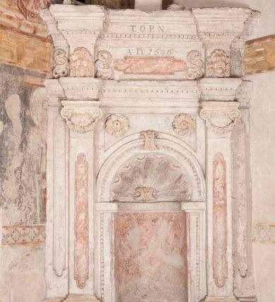 Zdjęcie nr 5: Zachowana dekoracja malarska znajduje się w tzw. starej zakrystii, określanej także jako oratorium królewskie. Dobudowano ją od północy do prezbiterium niepołomickiego kościoła. Jest to niewielka budowla na rzucie wydłużonego prostokąta, nakryta trójprzęsłowym krzyżowo-żebrowym sklepieniem, od wschodu zamknięta dwubocznie. Od zachodu w narożniku południowym widoczne jest załamanie muru, tworzącego dwie ściany wieżyczki schodowej. Do jej wnętrza prowadzi ostrołukowy portal. Oratorium oświetlają trzy ostrołukowe okna. Tylko czwarte, obecnie zamurowane, przeprute w murze północno-wschodnim pochodzi z czasów budowy kościoła. Stara zakrystia połączona jest z kościołem za pomocą ostrołukowego, profilowanego kamiennego portalu umieszczonego w środkowym przęśle ściany południowej. Na sklepieniu znajdują się rzeźbione zworniki z przedstawieniem w przęśle wschodnim głowy Chrystusa w nimbie krzyżowym, w środkowym maski liściastej, a w zachodnim motywów roślinnych. Podobnie rzeźbione motywy roślinne  pokrywają wsporniki, na które spływają żebra. 
Zachowana polichromia tworzy z architekturą starej zakrystii harmonijną całość. Białe wysklepki sklepień otoczone są wielobarwnymi, namalowanymi wzdłuż żeber, iluzjonistyczno-geometrycznymi pasami imitującymi kamienne inkrustacje w typie "arte cosmatesca". Pierwotnie polichromowane były także same żebra oraz rzeźbione zworniki i wsporniki. Pionowym rytmom barwnych pasów przeciwstawiają się na ścianie wschodniej, południowej i zachodniej dwa poziome, iluzjonistyczne malowane fryzy. Górny, w odcieniach brązów jest szerszy i przypomina gzyms. Przebiega w połowie wysokości ścian, na poziomie wsporników. Poniżej znajduje się drugi, o połowę węższy, skomponowany z wielobarwnych geometrycznych rozet w rombowych polach. Fryzy wyznaczają trzy strefy dekoracji. Dolny pas uległ zniszczeniu za wyjątkiem niewielkiego fragmentu iluzjonistycznie malowanej konsolki na ścianie południowej. Dla strefy środkowej głównej tło stanowi niebieska barwa. Niestety oba te pasy obecnie są mocno uszkodzone. 
Pierwotnie pas środkowy ścian zajmowały naturalnej wielkości postacie kobiece, ujęte powyżej kolan. Z namalowanych dwunastu świętych do naszych czasów przetrwało sześć - w całości cztery (na ścianie wschodniej, południowej i zachodniej) oraz jedna bez głowy (ściana południowa) i jedna w połowie (ściana zachodnia). Są to jasno lub ciemnowłose młode kobiety, trzymające palmy męczeństwa. Ubrane są w suknie z narzuconymi płaszczami w kolorach żółtym, oliwkowym, różowym, liliowym, brązowym i błękitnym. Jedna z nich, wyobrażona ponad wejściem na klatkę schodową w wieżyczce, jest ukazana jako kobieta w podeszłym wieku z okrytą głową i dłońmi uniesionymi na wysokość piersi w geście orantki. Głowy męczennic i orantki okalają plastycznie, tłoczone w zaprawie nimby zdobione promieniami. Na niektórych głowach dziewic zachowały się ślady namalowanych brązową farbą koron o niskich sterczynach w kształcie heraldycznych lilii. 
W ścianie północno-wschodniej dwubocznego zamknięcia znajduje się obecnie zamurowane lancetowate, ostrołukowe okno z fragmentami polichromii w glifie okiennym. Pierwotnie tworzyło ją dziesięć czterolistnych obramowań wpisanych w romby, umieszczonych jeden nad drugim. Przedstawiono w nich w półpostaci aniołów z głowami otoczonymi nimbami. W dolnej części okno do  poziomu gotyckich wsporników otacza iluzjonistycznie malowana dekoracja utworzona z motywów kamiennych płyt.  
W górnej strefie oratorium wyobrażono cykl hagiograficzny, składający się z sześciu scen namalowanych w ostrołukowych polach, wyznaczonych łukami tarczowymi sklepień i ujętych w obramienia z plastycznie malowanych zębów. Ograniczający je od dołu, iluzjonistycznie malowany, jakby wystający gzyms nadaje przedstawieniom teatralną głębie. 
Na ścianie południowo-wschodniej przedstawiono bliżej niezidentyfikowaną scenę męczeństwa. Na tle ochrowo-żółtej architektury ukazano z lewej strony na pierwszym planie grupę  rycerzy, z których dwóch widocznych jest w całej postaci w średniowiecznych zbrojach stylizowanych na rzymskie, w hełmach i z ostrołukowymi tarczami trzymanymi w lewych rękach. Ich odzież ma kolor błękitny, granatowy, czerwony, fioletowy, cynobrowy. Rycerze lekko unoszą głowy w stronę półpostaci wychylającej się z okna loggi w górnej części architektury. Był to zapewne władca, dziś jego postać zachowała się tylko fragmentarycznie. Postać z okna wskazuje palcem na centralnie ukazany kocioł zawieszony pod arkadą, stanowiącą część architektury tła. Widoczna w nim jest w półpostaci jasnowłosa kobieta w białej sukni na ramiączkach z modlitewnie złożonymi rękami na piersi. Jej głowę otacza nimb. Kocioł wisi na haku za półokrągły uchwyt, pod nim pali się ognisko. Z prawej strony kotła widoczna jest fragmentarycznie zachowana postać rycerza w zbroi, który oburącz długim kijem miesza w kotle. 
Na prawo od sceny męczeństwa na ścianie południowej namalowano scenę określaną jako "przed władcą". W centrum przedstawienia na tle architektury wyobrażono tron z zasiadającym na nim władcą. Jest to brodaty mężczyzna ukazany z profilu z koroną na głowie, który w prawej dłoni unosi berło skierowane w stronę przyprowadzonej do niego kobiety. Tron i architektoniczne jego obramienie malowane jest w kolorach brązu i ochry. Jego zaplecek dekoruje zawieszona pasiasta tkanina. Ciemnowłosy władca ubrany jest w turkusową szatę z narzuconym na ramiona brązowym płaszczem. Za tronem z lewej strony stoi paź o kędzierzawej fryzurze wsparty na trzymanym ostrzem w dół mieczu. Stojąca przed władcą kobieta ubrana jest w czerwoną długą suknię. Ma jasne włosy, a jej głowę okala nimb. Ręce ma skrzyżowane i związane na wysokości pasa. Obok niej stoi inna postać także w długiej szacie, z uniesioną prawą dłonią. Za świętą widoczne są inne postacie, niestety skala zniszczenia malowidła uniemożliwia ich opis i identyfikację. 
Trzecie malowidło, usytuowane nad wejściem do oratorium, ukazuje scenę dysputyt. W centrum przedstawienia pod architektonicznym zadaszeniem w formie portyku lub altany o kasetonowym stropie, wspartym na dwóch czworobocznych filarach, ukazano widoczne z profilu trzy siedzące  kobiety. Jedna z lewej strony a dwie naprzeciwko z prawej. Kobieta z lewej  ma odkryte jasne, długie włosy. Jej głowę otacza nimb. Na wysokość piersi unosi obie dłonie, sprawiając wrażenie, jakby w nich trzymała owalny przedmiot. Ubrana jest w ciemnoczerwoną długą suknię, zakrywającą nogi. Naprzeciw niej siedzą dwie inne niewiasty o długich, jasnych włosach w prostych koronach na głowach. Jedna z nich unosi swoją prawą rękę. Obie ubrane są w długie suknie w kolorze ochry. Za nimi pomiędzy filarami widoczna jest rozpięta zasłona w pionowe oliwkowe, zielone, białe i czerwone pasy. Na podłodze leży dywan dekorowany w żółte, zielone, niebieskie i czerwone pasy. 
Mocno zniszczone w dolnej części czwarte przedstawienie ilustruje scenę chłosty. Z lewej strony kompozycji wyobrażono budowlę z architektoniczną loggią, z której w półpostaci wychyla się władca. W prawej ręce poziomo trzyma berło skierowane w stronę grupy osób, za którymi wykonywana jest kara chłosty. Władca, podobnie jak w drugiej scenie, został ukazany jako mężczyzna o ciemnym zaroście i takich samych włosach. Na głowie ma koronę. Ubrany jest w brązowe szaty o różnych odcieniach. Centralnie przedstawioną stłoczoną grupę tworzy czterech żołnierzy oraz starszy mężczyzna w zawoju na głowie z siwą, długą brodą. Żołnierze mają zbroje i hełmy. Jeden z nich, najbliżej stojący z lewej przedstawiony został w profilu z głową i prawą ręką skierowaną w stronę króla. Także w stronę władcy zwrócony jest mężczyzna w zawoju na głowie z dwiema dłońmi uniesionymi na wysokość piersi. Z prawej strony kompozycji namalowano, dziś fragmentarycznie zachowany, rodzaj drewnianej szubienicy, utworzonej z poprzecznie zawieszonego na drewnianych podporach drążka. Nad dróżką do góry nogami wisi postać (dziś zniszczona), z której zachowały się jedynie stopy związane w kostkach sznurem. W jej stronę zwraca się jeden z żołnierzy ze środkowej grupy. Po prawej stronie szubienicy widoczna jest część postaci oprawcy, z której zachował się tylko fragment głowy oraz uniesiona lewa ręka z drewnianą pałką. 
Dwie ostatnie sceny umieszczono na zachodnim murze oratorium. Pierwsza z nich przedstawia strącenie bożka i została połączona z drugą ukazującą uwolnienia z więzienia. Część centralną kompozycji stanowi potrzaskana, wywracająca się kolumna, z której spada szatan w postaci żywego demona pokrytego sierścią. Strącił go widoczny w półpostaci w górnej części malowidła anioł trzymający w prawej ręce miecz. Z lewej strony kompozycji  klęczy na skalistej ziemi święta ubrana w długą ciemnoczerwoną suknię. Niestety nie zachowała się górna część jej postaci. Za nią stoi stłoczona grupa przerażonych świadków tego wydarzenia. Natomiast z prawej strony malowidła wyobrażono scenę uwolnienia z więzienia. Jej zasadniczym elementem jest architektoniczna struktura nawiązująca kształtem do wieży mieszkalnej, więzienia bądź bramy miejskiej. Święta ze związanymi rękami w ciemnoczerwonej sukni wychodzi z niej z prawej strony. W centrum budowli widoczne jest półokrągłe okno, a w nim zapewne jej popiersie o długich jasnych włosach, trzymające w dłoniach jakiś przedmiot. Wszystkie sceny cyklu w jedną całość wiąże gładkie niebieskie tło. Niezachowana kompozycja polichromii na ścianie północnej musiała odbiegać swym układem od pozostałych ścian. Płaszczyzna ścian została podzielona za pomocą węższego dolnego fryzu na dwie strefy. Górną część najprawdopodobniej zajmowały duże postacie stojące (fragment jednej z nich zachował się w sąsiedztwie okna w ścianie północno-wschodniej). Pod fryzem w części dolnej najprawdopodobniej była namalowana iluzjonistycznie wisząca kotara.   
    




