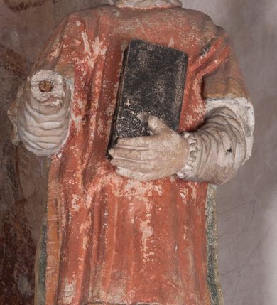 Zdjęcie nr 4: Zachowana dekoracja malarska znajduje się w tzw. starej zakrystii, określanej także jako oratorium królewskie. Dobudowano ją od północy do prezbiterium niepołomickiego kościoła. Jest to niewielka budowla na rzucie wydłużonego prostokąta, nakryta trójprzęsłowym krzyżowo-żebrowym sklepieniem, od wschodu zamknięta dwubocznie. Od zachodu w narożniku południowym widoczne jest załamanie muru, tworzącego dwie ściany wieżyczki schodowej. Do jej wnętrza prowadzi ostrołukowy portal. Oratorium oświetlają trzy ostrołukowe okna. Tylko czwarte, obecnie zamurowane, przeprute w murze północno-wschodnim pochodzi z czasów budowy kościoła. Stara zakrystia połączona jest z kościołem za pomocą ostrołukowego, profilowanego kamiennego portalu umieszczonego w środkowym przęśle ściany południowej. Na sklepieniu znajdują się rzeźbione zworniki z przedstawieniem w przęśle wschodnim głowy Chrystusa w nimbie krzyżowym, w środkowym maski liściastej, a w zachodnim motywów roślinnych. Podobnie rzeźbione motywy roślinne  pokrywają wsporniki, na które spływają żebra. 
Zachowana polichromia tworzy z architekturą starej zakrystii harmonijną całość. Białe wysklepki sklepień otoczone są wielobarwnymi, namalowanymi wzdłuż żeber, iluzjonistyczno-geometrycznymi pasami imitującymi kamienne inkrustacje w typie &quot;arte cosmatesca&quot;. Pierwotnie polichromowane były także same żebra oraz rzeźbione zworniki i wsporniki. Pionowym rytmom barwnych pasów przeciwstawiają się na ścianie wschodniej, południowej i zachodniej dwa poziome, iluzjonistyczne malowane fryzy. Górny, w odcieniach brązów jest szerszy i przypomina gzyms. Przebiega w połowie wysokości ścian, na poziomie wsporników. Poniżej znajduje się drugi, o połowę węższy, skomponowany z wielobarwnych geometrycznych rozet w rombowych polach. Fryzy wyznaczają trzy strefy dekoracji. Dolny pas uległ zniszczeniu za wyjątkiem niewielkiego fragmentu iluzjonistycznie malowanej konsolki na ścianie południowej. Dla strefy środkowej głównej tło stanowi niebieska barwa. Niestety oba te pasy obecnie są mocno uszkodzone. 
Pierwotnie pas środkowy ścian zajmowały naturalnej wielkości postacie kobiece, ujęte powyżej kolan. Z namalowanych dwunastu świętych do naszych czasów przetrwało sześć - w całości cztery (na ścianie wschodniej, południowej i zachodniej) oraz jedna bez głowy (ściana południowa) i jedna w połowie (ściana zachodnia). Są to jasno lub ciemnowłose młode kobiety, trzymające palmy męczeństwa. Ubrane są w suknie z narzuconymi płaszczami w kolorach żółtym, oliwkowym, różowym, liliowym, brązowym i błękitnym. Jedna z nich, wyobrażona ponad wejściem na klatkę schodową w wieżyczce, jest ukazana jako kobieta w podeszłym wieku z okrytą głową i dłońmi uniesionymi na wysokość piersi w geście orantki. Głowy męczennic i orantki okalają plastycznie, tłoczone w zaprawie nimby zdobione promieniami. Na niektórych głowach dziewic zachowały się ślady namalowanych brązową farbą koron o niskich sterczynach w kształcie heraldycznych lilii. 
W ścianie północno-wschodniej dwubocznego zamknięcia znajduje się obecnie zamurowane lancetowate, ostrołukowe okno z fragmentami polichromii w glifie okiennym. Pierwotnie tworzyło ją dziesięć czterolistnych obramowań wpisanych w romby, umieszczonych jeden nad drugim. Przedstawiono w nich w półpostaci aniołów z głowami otoczonymi nimbami. W dolnej części okno do  poziomu gotyckich wsporników otacza iluzjonistycznie malowana dekoracja utworzona z motywów kamiennych płyt.  
W górnej strefie oratorium wyobrażono cykl hagiograficzny, składający się z sześciu scen namalowanych w ostrołukowych polach, wyznaczonych łukami tarczowymi sklepień i ujętych w obramienia z plastycznie malowanych zębów. Ograniczający je od dołu, iluzjonistycznie malowany, jakby wystający gzyms nadaje przedstawieniom teatralną głębie. 
Na ścianie południowo-wschodniej przedstawiono bliżej niezidentyfikowaną scenę męczeństwa. Na tle ochrowo-żółtej architektury ukazano z lewej strony na pierwszym planie grupę  rycerzy, z których dwóch widocznych jest w całej postaci w średniowiecznych zbrojach stylizowanych na rzymskie, w hełmach i z ostrołukowymi tarczami trzymanymi w lewych rękach. Ich odzież ma kolor błękitny, granatowy, czerwony, fioletowy, cynobrowy. Rycerze lekko unoszą głowy w stronę półpostaci wychylającej się z okna loggi w górnej części architektury. Był to zapewne władca, dziś jego postać zachowała się tylko fragmentarycznie. Postać z okna wskazuje palcem na centralnie ukazany kocioł zawieszony pod arkadą, stanowiącą część architektury tła. Widoczna w nim jest w półpostaci jasnowłosa kobieta w białej sukni na ramiączkach z modlitewnie złożonymi rękami na piersi. Jej głowę otacza nimb. Kocioł wisi na haku za półokrągły uchwyt, pod nim pali się ognisko. Z prawej strony kotła widoczna jest fragmentarycznie zachowana postać rycerza w zbroi, który oburącz długim kijem miesza w kotle. 
Na prawo od sceny męczeństwa na ścianie południowej namalowano scenę określaną jako &quot;przed władcą&quot;. W centrum przedstawienia na tle architektury wyobrażono tron z zasiadającym na nim władcą. Jest to brodaty mężczyzna ukazany z profilu z koroną na głowie, który w prawej dłoni unosi berło skierowane w stronę przyprowadzonej do niego kobiety. Tron i architektoniczne jego obramienie malowane jest w kolorach brązu i ochry. Jego zaplecek dekoruje zawieszona pasiasta tkanina. Ciemnowłosy władca ubrany jest w turkusową szatę z narzuconym na ramiona brązowym płaszczem. Za tronem z lewej strony stoi paź o kędzierzawej fryzurze wsparty na trzymanym ostrzem w dół mieczu. Stojąca przed władcą kobieta ubrana jest w czerwoną długą suknię. Ma jasne włosy, a jej głowę okala nimb. Ręce ma skrzyżowane i związane na wysokości pasa. Obok niej stoi inna postać także w długiej szacie, z uniesioną prawą dłonią. Za świętą widoczne są inne postacie, niestety skala zniszczenia malowidła uniemożliwia ich opis i identyfikację. 
Trzecie malowidło, usytuowane nad wejściem do oratorium, ukazuje scenę dysputyt. W centrum przedstawienia pod architektonicznym zadaszeniem w formie portyku lub altany o kasetonowym stropie, wspartym na dwóch czworobocznych filarach, ukazano widoczne z profilu trzy siedzące  kobiety. Jedna z lewej strony a dwie naprzeciwko z prawej. Kobieta z lewej  ma odkryte jasne, długie włosy. Jej głowę otacza nimb. Na wysokość piersi unosi obie dłonie, sprawiając wrażenie, jakby w nich trzymała owalny przedmiot. Ubrana jest w ciemnoczerwoną długą suknię, zakrywającą nogi. Naprzeciw niej siedzą dwie inne niewiasty o długich, jasnych włosach w prostych koronach na głowach. Jedna z nich unosi swoją prawą rękę. Obie ubrane są w długie suknie w kolorze ochry. Za nimi pomiędzy filarami widoczna jest rozpięta zasłona w pionowe oliwkowe, zielone, białe i czerwone pasy. Na podłodze leży dywan dekorowany w żółte, zielone, niebieskie i czerwone pasy. 
Mocno zniszczone w dolnej części czwarte przedstawienie ilustruje scenę chłosty. Z lewej strony kompozycji wyobrażono budowlę z architektoniczną loggią, z której w półpostaci wychyla się władca. W prawej ręce poziomo trzyma berło skierowane w stronę grupy osób, za którymi wykonywana jest kara chłosty. Władca, podobnie jak w drugiej scenie, został ukazany jako mężczyzna o ciemnym zaroście i takich samych włosach. Na głowie ma koronę. Ubrany jest w brązowe szaty o różnych odcieniach. Centralnie przedstawioną stłoczoną grupę tworzy czterech żołnierzy oraz starszy mężczyzna w zawoju na głowie z siwą, długą brodą. Żołnierze mają zbroje i hełmy. Jeden z nich, najbliżej stojący z lewej przedstawiony został w profilu z głową i prawą ręką skierowaną w stronę króla. Także w stronę władcy zwrócony jest mężczyzna w zawoju na głowie z dwiema dłońmi uniesionymi na wysokość piersi. Z prawej strony kompozycji namalowano, dziś fragmentarycznie zachowany, rodzaj drewnianej szubienicy, utworzonej z poprzecznie zawieszonego na drewnianych podporach drążka. Nad dróżką do góry nogami wisi postać (dziś zniszczona), z której zachowały się jedynie stopy związane w kostkach sznurem. W jej stronę zwraca się jeden z żołnierzy ze środkowej grupy. Po prawej stronie szubienicy widoczna jest część postaci oprawcy, z której zachował się tylko fragment głowy oraz uniesiona lewa ręka z drewnianą pałką. 
Dwie ostatnie sceny umieszczono na zachodnim murze oratorium. Pierwsza z nich przedstawia strącenie bożka i została połączona z drugą ukazującą uwolnienia z więzienia. Część centralną kompozycji stanowi potrzaskana, wywracająca się kolumna, z której spada szatan w postaci żywego demona pokrytego sierścią. Strącił go widoczny w półpostaci w górnej części malowidła anioł trzymający w prawej ręce miecz. Z lewej strony kompozycji  klęczy na skalistej ziemi święta ubrana w długą ciemnoczerwoną suknię. Niestety nie zachowała się górna część jej postaci. Za nią stoi stłoczona grupa przerażonych świadków tego wydarzenia. Natomiast z prawej strony malowidła wyobrażono scenę uwolnienia z więzienia. Jej zasadniczym elementem jest architektoniczna struktura nawiązująca kształtem do wieży mieszkalnej, więzienia bądź bramy miejskiej. Święta ze związanymi rękami w ciemnoczerwonej sukni wychodzi z niej z prawej strony. W centrum budowli widoczne jest półokrągłe okno, a w nim zapewne jej popiersie o długich jasnych włosach, trzymające w dłoniach jakiś przedmiot. Wszystkie sceny cyklu w jedną całość wiąże gładkie niebieskie tło. Niezachowana kompozycja polichromii na ścianie północnej musiała odbiegać swym układem od pozostałych ścian. Płaszczyzna ścian została podzielona za pomocą węższego dolnego fryzu na dwie strefy. Górną część najprawdopodobniej zajmowały duże postacie stojące (fragment jednej z nich zachował się w sąsiedztwie okna w ścianie północno-wschodniej). Pod fryzem w części dolnej najprawdopodobniej była namalowana iluzjonistycznie wisząca kotara.   
    




