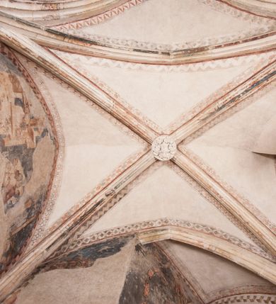 Zdjęcie nr 25: Zachowana dekoracja malarska znajduje się w tzw. starej zakrystii, określanej także jako oratorium królewskie. Dobudowano ją od północy do prezbiterium niepołomickiego kościoła. Jest to niewielka budowla na rzucie wydłużonego prostokąta, nakryta trójprzęsłowym krzyżowo-żebrowym sklepieniem, od wschodu zamknięta dwubocznie. Od zachodu w narożniku południowym widoczne jest załamanie muru, tworzącego dwie ściany wieżyczki schodowej. Do jej wnętrza prowadzi ostrołukowy portal. Oratorium oświetlają trzy ostrołukowe okna. Tylko czwarte, obecnie zamurowane, przeprute w murze północno-wschodnim pochodzi z czasów budowy kościoła. Stara zakrystia połączona jest z kościołem za pomocą ostrołukowego, profilowanego kamiennego portalu umieszczonego w środkowym przęśle ściany południowej. Na sklepieniu znajdują się rzeźbione zworniki z przedstawieniem w przęśle wschodnim głowy Chrystusa w nimbie krzyżowym, w środkowym maski liściastej, a w zachodnim motywów roślinnych. Podobnie rzeźbione motywy roślinne  pokrywają wsporniki, na które spływają żebra. 
Zachowana polichromia tworzy z architekturą starej zakrystii harmonijną całość. Białe wysklepki sklepień otoczone są wielobarwnymi, namalowanymi wzdłuż żeber, iluzjonistyczno-geometrycznymi pasami imitującymi kamienne inkrustacje w typie "arte cosmatesca". Pierwotnie polichromowane były także same żebra oraz rzeźbione zworniki i wsporniki. Pionowym rytmom barwnych pasów przeciwstawiają się na ścianie wschodniej, południowej i zachodniej dwa poziome, iluzjonistyczne malowane fryzy. Górny, w odcieniach brązów jest szerszy i przypomina gzyms. Przebiega w połowie wysokości ścian, na poziomie wsporników. Poniżej znajduje się drugi, o połowę węższy, skomponowany z wielobarwnych geometrycznych rozet w rombowych polach. Fryzy wyznaczają trzy strefy dekoracji. Dolny pas uległ zniszczeniu za wyjątkiem niewielkiego fragmentu iluzjonistycznie malowanej konsolki na ścianie południowej. Dla strefy środkowej głównej tło stanowi niebieska barwa. Niestety oba te pasy obecnie są mocno uszkodzone. 
Pierwotnie pas środkowy ścian zajmowały naturalnej wielkości postacie kobiece, ujęte powyżej kolan. Z namalowanych dwunastu świętych do naszych czasów przetrwało sześć - w całości cztery (na ścianie wschodniej, południowej i zachodniej) oraz jedna bez głowy (ściana południowa) i jedna w połowie (ściana zachodnia). Są to jasno lub ciemnowłose młode kobiety, trzymające palmy męczeństwa. Ubrane są w suknie z narzuconymi płaszczami w kolorach żółtym, oliwkowym, różowym, liliowym, brązowym i błękitnym. Jedna z nich, wyobrażona ponad wejściem na klatkę schodową w wieżyczce, jest ukazana jako kobieta w podeszłym wieku z okrytą głową i dłońmi uniesionymi na wysokość piersi w geście orantki. Głowy męczennic i orantki okalają plastycznie, tłoczone w zaprawie nimby zdobione promieniami. Na niektórych głowach dziewic zachowały się ślady namalowanych brązową farbą koron o niskich sterczynach w kształcie heraldycznych lilii. 
W ścianie północno-wschodniej dwubocznego zamknięcia znajduje się obecnie zamurowane lancetowate, ostrołukowe okno z fragmentami polichromii w glifie okiennym. Pierwotnie tworzyło ją dziesięć czterolistnych obramowań wpisanych w romby, umieszczonych jeden nad drugim. Przedstawiono w nich w półpostaci aniołów z głowami otoczonymi nimbami. W dolnej części okno do  poziomu gotyckich wsporników otacza iluzjonistycznie malowana dekoracja utworzona z motywów kamiennych płyt.  
W górnej strefie oratorium wyobrażono cykl hagiograficzny, składający się z sześciu scen namalowanych w ostrołukowych polach, wyznaczonych łukami tarczowymi sklepień i ujętych w obramienia z plastycznie malowanych zębów. Ograniczający je od dołu, iluzjonistycznie malowany, jakby wystający gzyms nadaje przedstawieniom teatralną głębie. 
Na ścianie południowo-wschodniej przedstawiono bliżej niezidentyfikowaną scenę męczeństwa. Na tle ochrowo-żółtej architektury ukazano z lewej strony na pierwszym planie grupę  rycerzy, z których dwóch widocznych jest w całej postaci w średniowiecznych zbrojach stylizowanych na rzymskie, w hełmach i z ostrołukowymi tarczami trzymanymi w lewych rękach. Ich odzież ma kolor błękitny, granatowy, czerwony, fioletowy, cynobrowy. Rycerze lekko unoszą głowy w stronę półpostaci wychylającej się z okna loggi w górnej części architektury. Był to zapewne władca, dziś jego postać zachowała się tylko fragmentarycznie. Postać z okna wskazuje palcem na centralnie ukazany kocioł zawieszony pod arkadą, stanowiącą część architektury tła. Widoczna w nim jest w półpostaci jasnowłosa kobieta w białej sukni na ramiączkach z modlitewnie złożonymi rękami na piersi. Jej głowę otacza nimb. Kocioł wisi na haku za półokrągły uchwyt, pod nim pali się ognisko. Z prawej strony kotła widoczna jest fragmentarycznie zachowana postać rycerza w zbroi, który oburącz długim kijem miesza w kotle. 
Na prawo od sceny męczeństwa na ścianie południowej namalowano scenę określaną jako "przed władcą". W centrum przedstawienia na tle architektury wyobrażono tron z zasiadającym na nim władcą. Jest to brodaty mężczyzna ukazany z profilu z koroną na głowie, który w prawej dłoni unosi berło skierowane w stronę przyprowadzonej do niego kobiety. Tron i architektoniczne jego obramienie malowane jest w kolorach brązu i ochry. Jego zaplecek dekoruje zawieszona pasiasta tkanina. Ciemnowłosy władca ubrany jest w turkusową szatę z narzuconym na ramiona brązowym płaszczem. Za tronem z lewej strony stoi paź o kędzierzawej fryzurze wsparty na trzymanym ostrzem w dół mieczu. Stojąca przed władcą kobieta ubrana jest w czerwoną długą suknię. Ma jasne włosy, a jej głowę okala nimb. Ręce ma skrzyżowane i związane na wysokości pasa. Obok niej stoi inna postać także w długiej szacie, z uniesioną prawą dłonią. Za świętą widoczne są inne postacie, niestety skala zniszczenia malowidła uniemożliwia ich opis i identyfikację. 
Trzecie malowidło, usytuowane nad wejściem do oratorium, ukazuje scenę dysputyt. W centrum przedstawienia pod architektonicznym zadaszeniem w formie portyku lub altany o kasetonowym stropie, wspartym na dwóch czworobocznych filarach, ukazano widoczne z profilu trzy siedzące  kobiety. Jedna z lewej strony a dwie naprzeciwko z prawej. Kobieta z lewej  ma odkryte jasne, długie włosy. Jej głowę otacza nimb. Na wysokość piersi unosi obie dłonie, sprawiając wrażenie, jakby w nich trzymała owalny przedmiot. Ubrana jest w ciemnoczerwoną długą suknię, zakrywającą nogi. Naprzeciw niej siedzą dwie inne niewiasty o długich, jasnych włosach w prostych koronach na głowach. Jedna z nich unosi swoją prawą rękę. Obie ubrane są w długie suknie w kolorze ochry. Za nimi pomiędzy filarami widoczna jest rozpięta zasłona w pionowe oliwkowe, zielone, białe i czerwone pasy. Na podłodze leży dywan dekorowany w żółte, zielone, niebieskie i czerwone pasy. 
Mocno zniszczone w dolnej części czwarte przedstawienie ilustruje scenę chłosty. Z lewej strony kompozycji wyobrażono budowlę z architektoniczną loggią, z której w półpostaci wychyla się władca. W prawej ręce poziomo trzyma berło skierowane w stronę grupy osób, za którymi wykonywana jest kara chłosty. Władca, podobnie jak w drugiej scenie, został ukazany jako mężczyzna o ciemnym zaroście i takich samych włosach. Na głowie ma koronę. Ubrany jest w brązowe szaty o różnych odcieniach. Centralnie przedstawioną stłoczoną grupę tworzy czterech żołnierzy oraz starszy mężczyzna w zawoju na głowie z siwą, długą brodą. Żołnierze mają zbroje i hełmy. Jeden z nich, najbliżej stojący z lewej przedstawiony został w profilu z głową i prawą ręką skierowaną w stronę króla. Także w stronę władcy zwrócony jest mężczyzna w zawoju na głowie z dwiema dłońmi uniesionymi na wysokość piersi. Z prawej strony kompozycji namalowano, dziś fragmentarycznie zachowany, rodzaj drewnianej szubienicy, utworzonej z poprzecznie zawieszonego na drewnianych podporach drążka. Nad dróżką do góry nogami wisi postać (dziś zniszczona), z której zachowały się jedynie stopy związane w kostkach sznurem. W jej stronę zwraca się jeden z żołnierzy ze środkowej grupy. Po prawej stronie szubienicy widoczna jest część postaci oprawcy, z której zachował się tylko fragment głowy oraz uniesiona lewa ręka z drewnianą pałką. 
Dwie ostatnie sceny umieszczono na zachodnim murze oratorium. Pierwsza z nich przedstawia strącenie bożka i została połączona z drugą ukazującą uwolnienia z więzienia. Część centralną kompozycji stanowi potrzaskana, wywracająca się kolumna, z której spada szatan w postaci żywego demona pokrytego sierścią. Strącił go widoczny w półpostaci w górnej części malowidła anioł trzymający w prawej ręce miecz. Z lewej strony kompozycji  klęczy na skalistej ziemi święta ubrana w długą ciemnoczerwoną suknię. Niestety nie zachowała się górna część jej postaci. Za nią stoi stłoczona grupa przerażonych świadków tego wydarzenia. Natomiast z prawej strony malowidła wyobrażono scenę uwolnienia z więzienia. Jej zasadniczym elementem jest architektoniczna struktura nawiązująca kształtem do wieży mieszkalnej, więzienia bądź bramy miejskiej. Święta ze związanymi rękami w ciemnoczerwonej sukni wychodzi z niej z prawej strony. W centrum budowli widoczne jest półokrągłe okno, a w nim zapewne jej popiersie o długich jasnych włosach, trzymające w dłoniach jakiś przedmiot. Wszystkie sceny cyklu w jedną całość wiąże gładkie niebieskie tło. Niezachowana kompozycja polichromii na ścianie północnej musiała odbiegać swym układem od pozostałych ścian. Płaszczyzna ścian została podzielona za pomocą węższego dolnego fryzu na dwie strefy. Górną część najprawdopodobniej zajmowały duże postacie stojące (fragment jednej z nich zachował się w sąsiedztwie okna w ścianie północno-wschodniej). Pod fryzem w części dolnej najprawdopodobniej była namalowana iluzjonistycznie wisząca kotara.   
    




