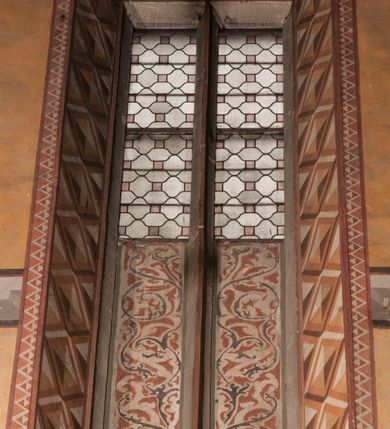 Zdjęcie nr 8: Malowidła z przedstawieniem św. Michała Archanioła pokonującego szatana i św. Jerzego walczącego ze smokiem zostały wykonane na ścianie północnej w dwóch wnękach podokiennych. Obie kompozycje powstały w polach o kształcie wydłużonego prostokąta. Święty Michał Archanioł został przedstawiony frontalnie w całej postaci z głową w ujęciu trzech czwartych w lewo. W uniesionej ponad głowę prawej ręce trzyma włócznię, wbitą w deptanego pod nogami szatana, którą jednocześnie podtrzymuje lewą ręką. Z tyłu widać jego rozpostarte skrzydła, skrzyżowane nad głową. Archanioł ma owalną twarz o wydatnym nosie oraz jasne włosy spływające na ramiona. Ubrany jest w przepasaną  tunikę sięgającą goleni i w narzucony na ramiona płaszcz. Postać diabła pod jego stopami obutymi w buty jest prawie niewidoczna. W podobny sposób przedstawiono św. Jerzego. Święty został ukazany frontalnie na rozstawionych nogach w całej postaci ujętej w kontrapoście z głową w trzech czwartych skierowaną w lewo. Prawą rękę ma uniesioną ponad głową i zgiętą w łokciu. Trzyma w niej lancę podtrzymywaną lewą ręką. Pod jego stopami widoczny jest zarys zwiniętego smoka o zarysie bazyliszka. Św. Jerzy ubrany jest w strój rycerski. Na głowie ma spiczasto zakończony hełm z kolczugą. Ciało okrywa mocno taliowana w pasie tunika zdobiona u dołu ornamentem z motywem trójkąta równoramiennego. Na nogach ma założone wysokie buty. W obu przedstawieniach widoczne są ciemne ugry, ciemna czerwień, żółcień, błękit i brąz. Tła są szare. 