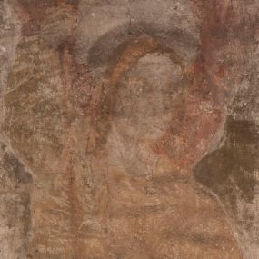 Zdjęcie nr 1: Malowidła z przedstawieniem św. Michała Archanioła pokonującego szatana i św. Jerzego walczącego ze smokiem zostały wykonane na ścianie północnej w dwóch wnękach podokiennych. Obie kompozycje powstały w polach o kształcie wydłużonego prostokąta. Święty Michał Archanioł został przedstawiony frontalnie w całej postaci z głową w ujęciu trzech czwartych w lewo. W uniesionej ponad głowę prawej ręce trzyma włócznię, wbitą w deptanego pod nogami szatana, którą jednocześnie podtrzymuje lewą ręką. Z tyłu widać jego rozpostarte skrzydła, skrzyżowane nad głową. Archanioł ma owalną twarz o wydatnym nosie oraz jasne włosy spływające na ramiona. Ubrany jest w przepasaną  tunikę sięgającą goleni i w narzucony na ramiona płaszcz. Postać diabła pod jego stopami obutymi w buty jest prawie niewidoczna. W podobny sposób przedstawiono św. Jerzego. Święty został ukazany frontalnie na rozstawionych nogach w całej postaci ujętej w kontrapoście z głową w trzech czwartych skierowaną w lewo. Prawą rękę ma uniesioną ponad głową i zgiętą w łokciu. Trzyma w niej lancę podtrzymywaną lewą ręką. Pod jego stopami widoczny jest zarys zwiniętego smoka o zarysie bazyliszka. Św. Jerzy ubrany jest w strój rycerski. Na głowie ma spiczasto zakończony hełm z kolczugą. Ciało okrywa mocno taliowana w pasie tunika zdobiona u dołu ornamentem z motywem trójkąta równoramiennego. Na nogach ma założone wysokie buty. W obu przedstawieniach widoczne są ciemne ugry, ciemna czerwień, żółcień, błękit i brąz. Tła są szare. 