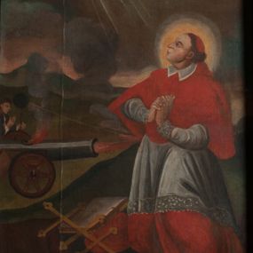 Zdjęcie nr 1: Obraz ma kształt stojącego prostokąta zamkniętego łukiem pełnym. Na tle pagórkowatego pejzażu z pochmurnym niebem oraz widocznymi w prawym górnym rogu złotymi promieniami, ukazano modlącego się św. Karola Boromeusza. Święty został przedstawiony z nieznacznie zgiętymi kolanami. Zwrócony jest w trzech czwartych w prawo, z głową ukazaną z profilu, lekko uniesioną wzwyż. Ręce ma złożone do modlitwy na wysokości piersi. Jego twarz zdradza rysy mężczyzny w średnim wieku z dużym, zakrzywionym nosem, lekko uśmiechniętymi ustami i wpatrzonymi wzwyż oczami. Twarz jest okolona krótkimi, brązowymi włosami. Boromeusz ubrany jest w strój kardynalski – purpurową sutannę, mucet, piuskę oraz białą komżę. W prawym, dolnym rogu obrazu u stóp świętego leży metropolitalny krzyż, zamknięta księga i kapelusz kardynalski. Powyżej, na drugim planie widoczny jest mężczyzna odpalający lont w strzelającej armacie wymierzonej w stronę modlącego się świętego. Dodatkowo zaznaczono trajektorię lotu odbitej kuli, widocznej obok głowy strzelającego. Zamachowiec ukazany jest w półpostaci, z odkrytą głową o brązowych włosach i twarzą ukazaną w profilu. Ubrany jest w ciemny mundur. Na stiukowej archiwolcie arkady umieszczono łaciński napis: „Non tanget illos tormentum mortis Sap[ientiae]: cap[ut]: 3 vers[us]: 1”. Napis po polsku umieszczono na dolnej krawędzi arkady: „Od Karola się kula z półhaku odbija / Wszak krzykiem Bóg i cnotą złość go łudzi”.