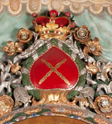 Zdjęcie nr 29: Obraz w formie stojącego prostokąta zamkniętego łukiem półkolistym. W centrum siedząca Matka Boska ukazana do kolan, frontalnie, lewym ramieniem obejmuje siedzące na jej kolanie Dzieciątko, w prawej ręce z przodu trzyma berło. Twarz ma owalną, o delikatnych rysach, dużych, migdałowatych oczach, długim, prostym nosie i niewielkich, pełnych ustach, okoloną długimi brązowymi włosami, opadającymi na ramiona. Ubrana jest w różową suknię, marszczoną przy dekolcie, z dekoracyjną lamówką oraz w obfity ciemnoniebieski płaszcz zarzucony na ramiona i opadający na kolana, ze złoconą lamówką i gwiazdą na prawym barku. Na głowie ma koronę otwartą, wokół nimb gwieździsty. Dzieciątko w pozycji siedzącej, zwrócone w trzech czwartych w prawo, w lewej ręce trzyma jabłko królewskie, prawą unosi w geście błogosławieństwa. Twarz ma kwadratową o pełnych policzkach, migdałowatych oczach, małym nosie i pełnych ustach, okoloną jasnymi, kręconymi włosami. Ubrane jest w fioletową tunikę oraz czerwony płaszcz przerzucony przez kolana. Na głowie ma koronę otwartą. Postacie ukazane na pomarańczowo-brązowym tle, koncentrycznie rozjaśnionym wokół głowy Marii, którą flankują dwa niewielkie anioły z rękami złożonymi w geście modlitwy. Obraz ujęty ornamentalną ramą utworzoną z wici roślinnej przeplatanej kwiatami, tworzącą nad łukiem szczyt z medalionem w wieńcu laurowym, ze skrzyżowanymi laskami marszałkowskimi w polu zwieńczonym koroną zamkniętą. W dolnej partii ramy płaskorzeźbione przedstawienie Chrystusa i Samarytanki przy studni z inicjałami „T(homas) O(linski) D(ecanus) W(ielicensis) P(lebanus) N(iepolomicensis) V(ir) I(llustris)”. 

