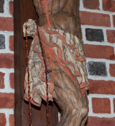 Zdjęcie nr 4: Pełnoplastyczna figura Chrystusa umarłego przybitego do krzyża o prostym zakończeniu ramion trzema gwoździami. Postać w lekkim zwisie, o szeroko rozłożonych ramionach, głowa opada na prawe ramię, nogi ugięte w kolanach, stopy skrzyżowane w układzie prawa na lewą. Jezus ma pociągłą twarz o dużych, zamkniętych oczach, prostym nosie i rozchylonych, wąskich ustach, okoloną falowaną, rozdwajającą się brodą oraz falowanymi, długimi włosami w formie pojedynczych pukli. Na głowie szeroka korona cierniowa. Ciało smukłe, wydłużone, z podkreśloną muskulaturą klatki piersiowej, pokryte siecią żył, z brodzącą rzeźbionymi kroplami krwi raną w boku. Perizonium sięgające połowy uda, zawiązane na prawym biodrze ze zwisem tkaniny, lamowane frędzlą. Ciało o ciemnej karnacji, z zaznaczonymi śladami męki, perizonium polichromowane na biało z wzorem w pasy. Pionowa belka krzyża zakończona rollwerkiem z uskrzydloną główką anielską z napisem „INRI”. 
Krucyfiks umieszczony w arkadzie ujętej pilastrami, dźwigającymi belkowanie. W partii fryzu napis „AGNUS MANSUETUS PORTATUR AD VICTIMAN”.