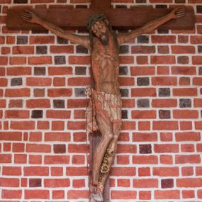 Zdjęcie nr 1: Pełnoplastyczna figura Chrystusa umarłego przybitego do krzyża o prostym zakończeniu ramion trzema gwoździami. Postać w lekkim zwisie, o szeroko rozłożonych ramionach, głowa opada na prawe ramię, nogi ugięte w kolanach, stopy skrzyżowane w układzie prawa na lewą. Jezus ma pociągłą twarz o dużych, zamkniętych oczach, prostym nosie i rozchylonych, wąskich ustach, okoloną falowaną, rozdwajającą się brodą oraz falowanymi, długimi włosami w formie pojedynczych pukli. Na głowie szeroka korona cierniowa. Ciało smukłe, wydłużone, z podkreśloną muskulaturą klatki piersiowej, pokryte siecią żył, z brodzącą rzeźbionymi kroplami krwi raną w boku. Perizonium sięgające połowy uda, zawiązane na prawym biodrze ze zwisem tkaniny, lamowane frędzlą. Ciało o ciemnej karnacji, z zaznaczonymi śladami męki, perizonium polichromowane na biało z wzorem w pasy. Pionowa belka krzyża zakończona rollwerkiem z uskrzydloną główką anielską z napisem „INRI”. 
Krucyfiks umieszczony w arkadzie ujętej pilastrami, dźwigającymi belkowanie. W partii fryzu napis „AGNUS MANSUETUS PORTATUR AD VICTIMAN”.