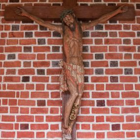 Zdjęcie nr 1: Pełnoplastyczna figura Chrystusa umarłego przybitego do krzyża o prostym zakończeniu ramion trzema gwoździami. Postać w lekkim zwisie, o szeroko rozłożonych ramionach, głowa opada na prawe ramię, nogi ugięte w kolanach, stopy skrzyżowane w układzie prawa na lewą. Jezus ma pociągłą twarz o dużych, zamkniętych oczach, prostym nosie i rozchylonych, wąskich ustach, okoloną falowaną, rozdwajającą się brodą oraz falowanymi, długimi włosami w formie pojedynczych pukli. Na głowie szeroka korona cierniowa. Ciało smukłe, wydłużone, z podkreśloną muskulaturą klatki piersiowej, pokryte siecią żył, z brodzącą rzeźbionymi kroplami krwi raną w boku. Perizonium sięgające połowy uda, zawiązane na prawym biodrze ze zwisem tkaniny, lamowane frędzlą. Ciało o ciemnej karnacji, z zaznaczonymi śladami męki, perizonium polichromowane na biało z wzorem w pasy. Pionowa belka krzyża zakończona rollwerkiem z uskrzydloną główką anielską z napisem „INRI”. 
Krucyfiks umieszczony w arkadzie ujętej pilastrami, dźwigającymi belkowanie. W partii fryzu napis „AGNUS MANSUETUS PORTATUR AD VICTIMAN”.