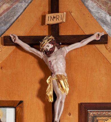 Zdjęcie nr 1: Figura Chrystusa umarłego przybitego do krzyża o prostych ramionach trzema gwoździami. Ciało w silnym zwisie, o szeroko rozłożonych ramionach, głowa opadająca na prawy bark, nogi ugięte w kolanach, stopy skrzyżowane w układzie prawa na lewą. Jezus ma kwadratową twarz, o zamkniętych oczach, małym nosie i pełnych ustach, okoloną krótką brodą i kręconymi, brązowymi włosami opadającymi na ramiona. Na głowie złocona korona cierniowa. Ciało szczupłe, o rozbudowanej i muskularnej klatce piersiowej z podkreślonymi żebrami. Złocone perizonium zawieszone na podwójnym sznurze, odsłaniające prawe biodro, ze zwisem tkaniny przy prawym boku. Polichromia ciała naturalistyczna z zaznaczonymi śladami męki. Na zakończeniu pionowej belki krzyża tabliczka z napisem „INRI”. 




