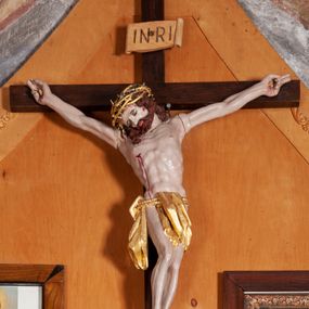 Zdjęcie nr 1: Figura Chrystusa umarłego przybitego do krzyża o prostych ramionach trzema gwoździami. Ciało w silnym zwisie, o szeroko rozłożonych ramionach, głowa opadająca na prawy bark, nogi ugięte w kolanach, stopy skrzyżowane w układzie prawa na lewą. Jezus ma kwadratową twarz, o zamkniętych oczach, małym nosie i pełnych ustach, okoloną krótką brodą i kręconymi, brązowymi włosami opadającymi na ramiona. Na głowie złocona korona cierniowa. Ciało szczupłe, o rozbudowanej i muskularnej klatce piersiowej z podkreślonymi żebrami. Złocone perizonium zawieszone na podwójnym sznurze, odsłaniające prawe biodro, ze zwisem tkaniny przy prawym boku. Polichromia ciała naturalistyczna z zaznaczonymi śladami męki. Na zakończeniu pionowej belki krzyża tabliczka z napisem „INRI”. 



