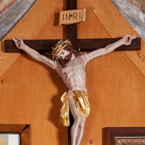 Zdjęcie nr 1: Figura Chrystusa umarłego przybitego do krzyża o prostych ramionach trzema gwoździami. Ciało w silnym zwisie, o szeroko rozłożonych ramionach, głowa opadająca na prawy bark, nogi ugięte w kolanach, stopy skrzyżowane w układzie prawa na lewą. Jezus ma kwadratową twarz, o zamkniętych oczach, małym nosie i pełnych ustach, okoloną krótką brodą i kręconymi, brązowymi włosami opadającymi na ramiona. Na głowie złocona korona cierniowa. Ciało szczupłe, o rozbudowanej i muskularnej klatce piersiowej z podkreślonymi żebrami. Złocone perizonium zawieszone na podwójnym sznurze, odsłaniające prawe biodro, ze zwisem tkaniny przy prawym boku. Polichromia ciała naturalistyczna z zaznaczonymi śladami męki. Na zakończeniu pionowej belki krzyża tabliczka z napisem „INRI”. 



