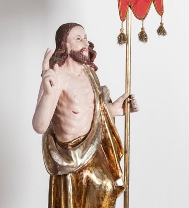 Zdjęcie nr 1: Pełnoplastyczna rzeźba przedstawia Chrystusa Zmartwychwstałego, stojącego w lekkim kontrapoście, z ciężarem ciała wspartym na lewej nodze, która depcze węża trzymającego w paszczy jabłko. Zbawiciel prawą nogę lekko ugina w kolanie opierając ją na ludzkiej czaszce. Chrystus w lewej ręce trzyma złotą laskę krzyżową z podwieszoną chorągwią, prawą zaś unosi w geście błogosławieństwa. Ma owalną twarz z prostym nosem, z uniesionymi ku górze brązowymi oczami i jasnoróżowymi ustami. Jego głowę okalają długie, brązowe włosy opadające na ramiona w lekkich lokach oraz krótka, brązowa broda. Zmartwychwstały ubrany jest w złocony płaszcz ze srebrną podszewką, odsłaniający prawe ramię, przerzucony z przodu przez lewą rękę i opadający miękkimi fałdami zakrywając prawy bok postaci. Karnacja ciała jest bladoróżowa. Na dłoniach, boku oraz stopach widoczne są czerwone rany po gwoździach i lancy. 