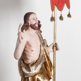 Zdjęcie nr 1: Pełnoplastyczna rzeźba przedstawia Chrystusa Zmartwychwstałego, stojącego w lekkim kontrapoście, z ciężarem ciała wspartym na lewej nodze, która depcze węża trzymającego w paszczy jabłko. Zbawiciel prawą nogę lekko ugina w kolanie opierając ją na ludzkiej czaszce. Chrystus w lewej ręce trzyma złotą laskę krzyżową z podwieszoną chorągwią, prawą zaś unosi w geście błogosławieństwa. Ma owalną twarz z prostym nosem, z uniesionymi ku górze brązowymi oczami i jasnoróżowymi ustami. Jego głowę okalają długie, brązowe włosy opadające na ramiona w lekkich lokach oraz krótka, brązowa broda. Zmartwychwstały ubrany jest w złocony płaszcz ze srebrną podszewką, odsłaniający prawe ramię, przerzucony z przodu przez lewą rękę i opadający miękkimi fałdami zakrywając prawy bok postaci. Karnacja ciała jest bladoróżowa. Na dłoniach, boku oraz stopach widoczne są czerwone rany po gwoździach i lancy. 