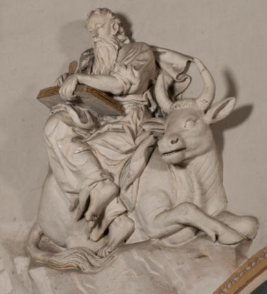 Zdjęcie nr 21: Pełnoplastyczna figura Chrystusa Ukrzyżowanego umieszczona jest na belce tęczowej. Chrystus został ukazany na krzyżu w dużym zwisie na wyprężonych ramionach, tworzących kształt litery „V”. Jego korpus jest wydłużony i esowato wygięty z silnym zaznaczeniem modelunku anatomicznego. Nogi zostały lekko zgięte w kolanach i nieznacznie odchylone w bok, zaś stopy skrzyżowane i przybite jednym gwoździem do krzyża. Wyeksponowano muskulaturę kończyn, żebra i ranę w boku. Głowa Zbawiciela opada na prawe ramię. Jego twarz jest podłużna, z długim, prostym nosem, o zamkniętych oczach i otwartych ustach w grymasie bólu. Otacza ją gęsta, kręcona broda oraz długie, ciemne włosy opadające lokami na oba ramiona. Na głowie widoczna jest cierniowa korona o długich kolcach. Biodra Zbawiciela zostały przepasane długim perizonium sięgającym kolan. Jest ono na środku drapowane za pomocą misowych fałd układających się poprzecznie, zaś po bokach zostało wywinięte za pomocą dwóch festonów opadających kaskadowo wzdłuż ud. Ponad głową Chrystusa umieszczony jest złocony titulus o kształtach barokowych w formie kartusza z napisem „INRI”.Rzeźba jest polichromowana, a perizonium srebrzone z zastosowaniem laserunków.