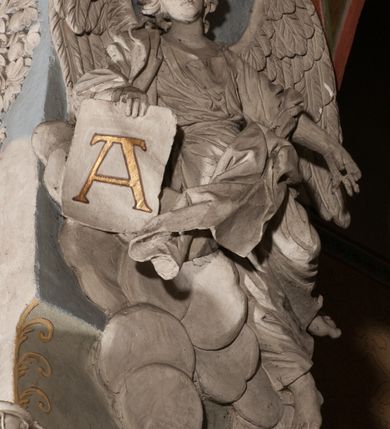 Zdjęcie nr 24: Pełnoplastyczna figura Chrystusa Ukrzyżowanego umieszczona jest na belce tęczowej. Chrystus został ukazany na krzyżu w dużym zwisie na wyprężonych ramionach, tworzących kształt litery „V”. Jego korpus jest wydłużony i esowato wygięty z silnym zaznaczeniem modelunku anatomicznego. Nogi zostały lekko zgięte w kolanach i nieznacznie odchylone w bok, zaś stopy skrzyżowane i przybite jednym gwoździem do krzyża. Wyeksponowano muskulaturę kończyn, żebra i ranę w boku. Głowa Zbawiciela opada na prawe ramię. Jego twarz jest podłużna, z długim, prostym nosem, o zamkniętych oczach i otwartych ustach w grymasie bólu. Otacza ją gęsta, kręcona broda oraz długie, ciemne włosy opadające lokami na oba ramiona. Na głowie widoczna jest cierniowa korona o długich kolcach. Biodra Zbawiciela zostały przepasane długim perizonium sięgającym kolan. Jest ono na środku drapowane za pomocą misowych fałd układających się poprzecznie, zaś po bokach zostało wywinięte za pomocą dwóch festonów opadających kaskadowo wzdłuż ud. Ponad głową Chrystusa umieszczony jest złocony titulus o kształtach barokowych w formie kartusza z napisem „INRI”.Rzeźba jest polichromowana, a perizonium srebrzone z zastosowaniem laserunków.