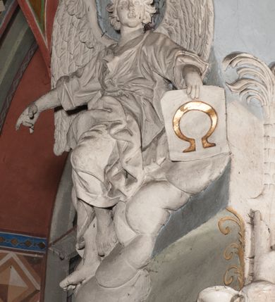 Zdjęcie nr 26: Pełnoplastyczna figura Chrystusa Ukrzyżowanego umieszczona jest na belce tęczowej. Chrystus został ukazany na krzyżu w dużym zwisie na wyprężonych ramionach, tworzących kształt litery „V”. Jego korpus jest wydłużony i esowato wygięty z silnym zaznaczeniem modelunku anatomicznego. Nogi zostały lekko zgięte w kolanach i nieznacznie odchylone w bok, zaś stopy skrzyżowane i przybite jednym gwoździem do krzyża. Wyeksponowano muskulaturę kończyn, żebra i ranę w boku. Głowa Zbawiciela opada na prawe ramię. Jego twarz jest podłużna, z długim, prostym nosem, o zamkniętych oczach i otwartych ustach w grymasie bólu. Otacza ją gęsta, kręcona broda oraz długie, ciemne włosy opadające lokami na oba ramiona. Na głowie widoczna jest cierniowa korona o długich kolcach. Biodra Zbawiciela zostały przepasane długim perizonium sięgającym kolan. Jest ono na środku drapowane za pomocą misowych fałd układających się poprzecznie, zaś po bokach zostało wywinięte za pomocą dwóch festonów opadających kaskadowo wzdłuż ud. Ponad głową Chrystusa umieszczony jest złocony titulus o kształtach barokowych w formie kartusza z napisem „INRI”.Rzeźba jest polichromowana, a perizonium srebrzone z zastosowaniem laserunków.