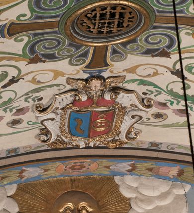 Zdjęcie nr 30: Pełnoplastyczna figura Chrystusa Ukrzyżowanego umieszczona jest na belce tęczowej. Chrystus został ukazany na krzyżu w dużym zwisie na wyprężonych ramionach, tworzących kształt litery „V”. Jego korpus jest wydłużony i esowato wygięty z silnym zaznaczeniem modelunku anatomicznego. Nogi zostały lekko zgięte w kolanach i nieznacznie odchylone w bok, zaś stopy skrzyżowane i przybite jednym gwoździem do krzyża. Wyeksponowano muskulaturę kończyn, żebra i ranę w boku. Głowa Zbawiciela opada na prawe ramię. Jego twarz jest podłużna, z długim, prostym nosem, o zamkniętych oczach i otwartych ustach w grymasie bólu. Otacza ją gęsta, kręcona broda oraz długie, ciemne włosy opadające lokami na oba ramiona. Na głowie widoczna jest cierniowa korona o długich kolcach. Biodra Zbawiciela zostały przepasane długim perizonium sięgającym kolan. Jest ono na środku drapowane za pomocą misowych fałd układających się poprzecznie, zaś po bokach zostało wywinięte za pomocą dwóch festonów opadających kaskadowo wzdłuż ud. Ponad głową Chrystusa umieszczony jest złocony titulus o kształtach barokowych w formie kartusza z napisem „INRI”.Rzeźba jest polichromowana, a perizonium srebrzone z zastosowaniem laserunków.