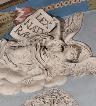 Zdjęcie nr 29: Pełnoplastyczna figura Chrystusa Ukrzyżowanego umieszczona jest na belce tęczowej. Chrystus został ukazany na krzyżu w dużym zwisie na wyprężonych ramionach, tworzących kształt litery „V”. Jego korpus jest wydłużony i esowato wygięty z silnym zaznaczeniem modelunku anatomicznego. Nogi zostały lekko zgięte w kolanach i nieznacznie odchylone w bok, zaś stopy skrzyżowane i przybite jednym gwoździem do krzyża. Wyeksponowano muskulaturę kończyn, żebra i ranę w boku. Głowa Zbawiciela opada na prawe ramię. Jego twarz jest podłużna, z długim, prostym nosem, o zamkniętych oczach i otwartych ustach w grymasie bólu. Otacza ją gęsta, kręcona broda oraz długie, ciemne włosy opadające lokami na oba ramiona. Na głowie widoczna jest cierniowa korona o długich kolcach. Biodra Zbawiciela zostały przepasane długim perizonium sięgającym kolan. Jest ono na środku drapowane za pomocą misowych fałd układających się poprzecznie, zaś po bokach zostało wywinięte za pomocą dwóch festonów opadających kaskadowo wzdłuż ud. Ponad głową Chrystusa umieszczony jest złocony titulus o kształtach barokowych w formie kartusza z napisem „INRI”.Rzeźba jest polichromowana, a perizonium srebrzone z zastosowaniem laserunków.