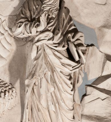 Zdjęcie nr 32: Pełnoplastyczna figura Chrystusa Ukrzyżowanego umieszczona jest na belce tęczowej. Chrystus został ukazany na krzyżu w dużym zwisie na wyprężonych ramionach, tworzących kształt litery „V”. Jego korpus jest wydłużony i esowato wygięty z silnym zaznaczeniem modelunku anatomicznego. Nogi zostały lekko zgięte w kolanach i nieznacznie odchylone w bok, zaś stopy skrzyżowane i przybite jednym gwoździem do krzyża. Wyeksponowano muskulaturę kończyn, żebra i ranę w boku. Głowa Zbawiciela opada na prawe ramię. Jego twarz jest podłużna, z długim, prostym nosem, o zamkniętych oczach i otwartych ustach w grymasie bólu. Otacza ją gęsta, kręcona broda oraz długie, ciemne włosy opadające lokami na oba ramiona. Na głowie widoczna jest cierniowa korona o długich kolcach. Biodra Zbawiciela zostały przepasane długim perizonium sięgającym kolan. Jest ono na środku drapowane za pomocą misowych fałd układających się poprzecznie, zaś po bokach zostało wywinięte za pomocą dwóch festonów opadających kaskadowo wzdłuż ud. Ponad głową Chrystusa umieszczony jest złocony titulus o kształtach barokowych w formie kartusza z napisem „INRI”.Rzeźba jest polichromowana, a perizonium srebrzone z zastosowaniem laserunków.