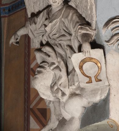 Zdjęcie nr 31: Pełnoplastyczna figura Chrystusa Ukrzyżowanego umieszczona jest na belce tęczowej. Chrystus został ukazany na krzyżu w dużym zwisie na wyprężonych ramionach, tworzących kształt litery „V”. Jego korpus jest wydłużony i esowato wygięty z silnym zaznaczeniem modelunku anatomicznego. Nogi zostały lekko zgięte w kolanach i nieznacznie odchylone w bok, zaś stopy skrzyżowane i przybite jednym gwoździem do krzyża. Wyeksponowano muskulaturę kończyn, żebra i ranę w boku. Głowa Zbawiciela opada na prawe ramię. Jego twarz jest podłużna, z długim, prostym nosem, o zamkniętych oczach i otwartych ustach w grymasie bólu. Otacza ją gęsta, kręcona broda oraz długie, ciemne włosy opadające lokami na oba ramiona. Na głowie widoczna jest cierniowa korona o długich kolcach. Biodra Zbawiciela zostały przepasane długim perizonium sięgającym kolan. Jest ono na środku drapowane za pomocą misowych fałd układających się poprzecznie, zaś po bokach zostało wywinięte za pomocą dwóch festonów opadających kaskadowo wzdłuż ud. Ponad głową Chrystusa umieszczony jest złocony titulus o kształtach barokowych w formie kartusza z napisem „INRI”.Rzeźba jest polichromowana, a perizonium srebrzone z zastosowaniem laserunków.