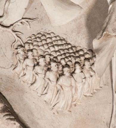 Zdjęcie nr 35: Pełnoplastyczna figura Chrystusa Ukrzyżowanego umieszczona jest na belce tęczowej. Chrystus został ukazany na krzyżu w dużym zwisie na wyprężonych ramionach, tworzących kształt litery „V”. Jego korpus jest wydłużony i esowato wygięty z silnym zaznaczeniem modelunku anatomicznego. Nogi zostały lekko zgięte w kolanach i nieznacznie odchylone w bok, zaś stopy skrzyżowane i przybite jednym gwoździem do krzyża. Wyeksponowano muskulaturę kończyn, żebra i ranę w boku. Głowa Zbawiciela opada na prawe ramię. Jego twarz jest podłużna, z długim, prostym nosem, o zamkniętych oczach i otwartych ustach w grymasie bólu. Otacza ją gęsta, kręcona broda oraz długie, ciemne włosy opadające lokami na oba ramiona. Na głowie widoczna jest cierniowa korona o długich kolcach. Biodra Zbawiciela zostały przepasane długim perizonium sięgającym kolan. Jest ono na środku drapowane za pomocą misowych fałd układających się poprzecznie, zaś po bokach zostało wywinięte za pomocą dwóch festonów opadających kaskadowo wzdłuż ud. Ponad głową Chrystusa umieszczony jest złocony titulus o kształtach barokowych w formie kartusza z napisem „INRI”.Rzeźba jest polichromowana, a perizonium srebrzone z zastosowaniem laserunków.