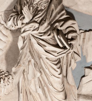 Zdjęcie nr 34: Pełnoplastyczna figura Chrystusa Ukrzyżowanego umieszczona jest na belce tęczowej. Chrystus został ukazany na krzyżu w dużym zwisie na wyprężonych ramionach, tworzących kształt litery „V”. Jego korpus jest wydłużony i esowato wygięty z silnym zaznaczeniem modelunku anatomicznego. Nogi zostały lekko zgięte w kolanach i nieznacznie odchylone w bok, zaś stopy skrzyżowane i przybite jednym gwoździem do krzyża. Wyeksponowano muskulaturę kończyn, żebra i ranę w boku. Głowa Zbawiciela opada na prawe ramię. Jego twarz jest podłużna, z długim, prostym nosem, o zamkniętych oczach i otwartych ustach w grymasie bólu. Otacza ją gęsta, kręcona broda oraz długie, ciemne włosy opadające lokami na oba ramiona. Na głowie widoczna jest cierniowa korona o długich kolcach. Biodra Zbawiciela zostały przepasane długim perizonium sięgającym kolan. Jest ono na środku drapowane za pomocą misowych fałd układających się poprzecznie, zaś po bokach zostało wywinięte za pomocą dwóch festonów opadających kaskadowo wzdłuż ud. Ponad głową Chrystusa umieszczony jest złocony titulus o kształtach barokowych w formie kartusza z napisem „INRI”.Rzeźba jest polichromowana, a perizonium srebrzone z zastosowaniem laserunków.