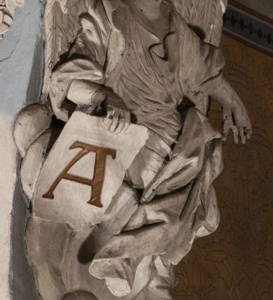 Zdjęcie nr 41: Pełnoplastyczna figura Chrystusa Ukrzyżowanego umieszczona jest na belce tęczowej. Chrystus został ukazany na krzyżu w dużym zwisie na wyprężonych ramionach, tworzących kształt litery „V”. Jego korpus jest wydłużony i esowato wygięty z silnym zaznaczeniem modelunku anatomicznego. Nogi zostały lekko zgięte w kolanach i nieznacznie odchylone w bok, zaś stopy skrzyżowane i przybite jednym gwoździem do krzyża. Wyeksponowano muskulaturę kończyn, żebra i ranę w boku. Głowa Zbawiciela opada na prawe ramię. Jego twarz jest podłużna, z długim, prostym nosem, o zamkniętych oczach i otwartych ustach w grymasie bólu. Otacza ją gęsta, kręcona broda oraz długie, ciemne włosy opadające lokami na oba ramiona. Na głowie widoczna jest cierniowa korona o długich kolcach. Biodra Zbawiciela zostały przepasane długim perizonium sięgającym kolan. Jest ono na środku drapowane za pomocą misowych fałd układających się poprzecznie, zaś po bokach zostało wywinięte za pomocą dwóch festonów opadających kaskadowo wzdłuż ud. Ponad głową Chrystusa umieszczony jest złocony titulus o kształtach barokowych w formie kartusza z napisem „INRI”.Rzeźba jest polichromowana, a perizonium srebrzone z zastosowaniem laserunków.