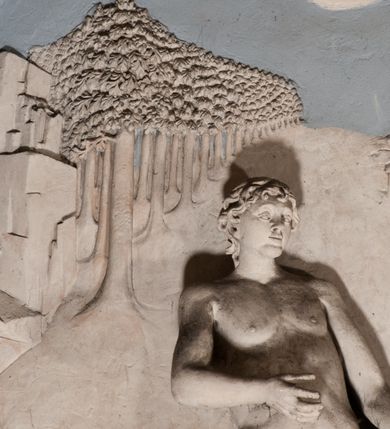 Zdjęcie nr 48: Pełnoplastyczna figura Chrystusa Ukrzyżowanego umieszczona jest na belce tęczowej. Chrystus został ukazany na krzyżu w dużym zwisie na wyprężonych ramionach, tworzących kształt litery „V”. Jego korpus jest wydłużony i esowato wygięty z silnym zaznaczeniem modelunku anatomicznego. Nogi zostały lekko zgięte w kolanach i nieznacznie odchylone w bok, zaś stopy skrzyżowane i przybite jednym gwoździem do krzyża. Wyeksponowano muskulaturę kończyn, żebra i ranę w boku. Głowa Zbawiciela opada na prawe ramię. Jego twarz jest podłużna, z długim, prostym nosem, o zamkniętych oczach i otwartych ustach w grymasie bólu. Otacza ją gęsta, kręcona broda oraz długie, ciemne włosy opadające lokami na oba ramiona. Na głowie widoczna jest cierniowa korona o długich kolcach. Biodra Zbawiciela zostały przepasane długim perizonium sięgającym kolan. Jest ono na środku drapowane za pomocą misowych fałd układających się poprzecznie, zaś po bokach zostało wywinięte za pomocą dwóch festonów opadających kaskadowo wzdłuż ud. Ponad głową Chrystusa umieszczony jest złocony titulus o kształtach barokowych w formie kartusza z napisem „INRI”.Rzeźba jest polichromowana, a perizonium srebrzone z zastosowaniem laserunków.