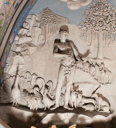 Zdjęcie nr 49: Pełnoplastyczna figura Chrystusa Ukrzyżowanego umieszczona jest na belce tęczowej. Chrystus został ukazany na krzyżu w dużym zwisie na wyprężonych ramionach, tworzących kształt litery „V”. Jego korpus jest wydłużony i esowato wygięty z silnym zaznaczeniem modelunku anatomicznego. Nogi zostały lekko zgięte w kolanach i nieznacznie odchylone w bok, zaś stopy skrzyżowane i przybite jednym gwoździem do krzyża. Wyeksponowano muskulaturę kończyn, żebra i ranę w boku. Głowa Zbawiciela opada na prawe ramię. Jego twarz jest podłużna, z długim, prostym nosem, o zamkniętych oczach i otwartych ustach w grymasie bólu. Otacza ją gęsta, kręcona broda oraz długie, ciemne włosy opadające lokami na oba ramiona. Na głowie widoczna jest cierniowa korona o długich kolcach. Biodra Zbawiciela zostały przepasane długim perizonium sięgającym kolan. Jest ono na środku drapowane za pomocą misowych fałd układających się poprzecznie, zaś po bokach zostało wywinięte za pomocą dwóch festonów opadających kaskadowo wzdłuż ud. Ponad głową Chrystusa umieszczony jest złocony titulus o kształtach barokowych w formie kartusza z napisem „INRI”.Rzeźba jest polichromowana, a perizonium srebrzone z zastosowaniem laserunków.