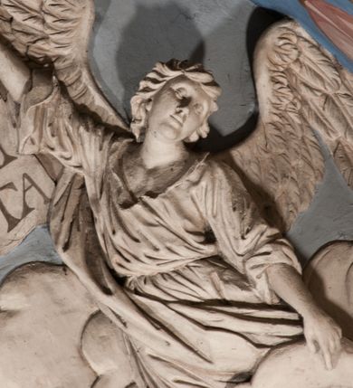 Zdjęcie nr 52: Pełnoplastyczna figura Chrystusa Ukrzyżowanego umieszczona jest na belce tęczowej. Chrystus został ukazany na krzyżu w dużym zwisie na wyprężonych ramionach, tworzących kształt litery „V”. Jego korpus jest wydłużony i esowato wygięty z silnym zaznaczeniem modelunku anatomicznego. Nogi zostały lekko zgięte w kolanach i nieznacznie odchylone w bok, zaś stopy skrzyżowane i przybite jednym gwoździem do krzyża. Wyeksponowano muskulaturę kończyn, żebra i ranę w boku. Głowa Zbawiciela opada na prawe ramię. Jego twarz jest podłużna, z długim, prostym nosem, o zamkniętych oczach i otwartych ustach w grymasie bólu. Otacza ją gęsta, kręcona broda oraz długie, ciemne włosy opadające lokami na oba ramiona. Na głowie widoczna jest cierniowa korona o długich kolcach. Biodra Zbawiciela zostały przepasane długim perizonium sięgającym kolan. Jest ono na środku drapowane za pomocą misowych fałd układających się poprzecznie, zaś po bokach zostało wywinięte za pomocą dwóch festonów opadających kaskadowo wzdłuż ud. Ponad głową Chrystusa umieszczony jest złocony titulus o kształtach barokowych w formie kartusza z napisem „INRI”.Rzeźba jest polichromowana, a perizonium srebrzone z zastosowaniem laserunków.