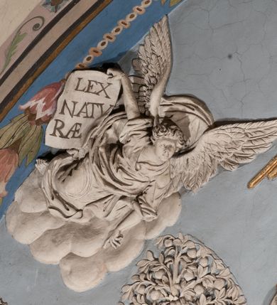 Zdjęcie nr 55: Pełnoplastyczna figura Chrystusa Ukrzyżowanego umieszczona jest na belce tęczowej. Chrystus został ukazany na krzyżu w dużym zwisie na wyprężonych ramionach, tworzących kształt litery „V”. Jego korpus jest wydłużony i esowato wygięty z silnym zaznaczeniem modelunku anatomicznego. Nogi zostały lekko zgięte w kolanach i nieznacznie odchylone w bok, zaś stopy skrzyżowane i przybite jednym gwoździem do krzyża. Wyeksponowano muskulaturę kończyn, żebra i ranę w boku. Głowa Zbawiciela opada na prawe ramię. Jego twarz jest podłużna, z długim, prostym nosem, o zamkniętych oczach i otwartych ustach w grymasie bólu. Otacza ją gęsta, kręcona broda oraz długie, ciemne włosy opadające lokami na oba ramiona. Na głowie widoczna jest cierniowa korona o długich kolcach. Biodra Zbawiciela zostały przepasane długim perizonium sięgającym kolan. Jest ono na środku drapowane za pomocą misowych fałd układających się poprzecznie, zaś po bokach zostało wywinięte za pomocą dwóch festonów opadających kaskadowo wzdłuż ud. Ponad głową Chrystusa umieszczony jest złocony titulus o kształtach barokowych w formie kartusza z napisem „INRI”.Rzeźba jest polichromowana, a perizonium srebrzone z zastosowaniem laserunków.