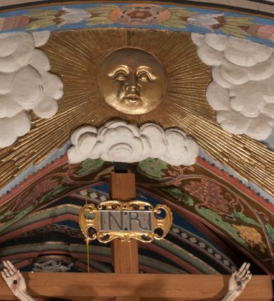 Zdjęcie nr 17: Pełnoplastyczna figura Chrystusa Ukrzyżowanego umieszczona jest na belce tęczowej. Chrystus został ukazany na krzyżu w dużym zwisie na wyprężonych ramionach, tworzących kształt litery „V”. Jego korpus jest wydłużony i esowato wygięty z silnym zaznaczeniem modelunku anatomicznego. Nogi zostały lekko zgięte w kolanach i nieznacznie odchylone w bok, zaś stopy skrzyżowane i przybite jednym gwoździem do krzyża. Wyeksponowano muskulaturę kończyn, żebra i ranę w boku. Głowa Zbawiciela opada na prawe ramię. Jego twarz jest podłużna, z długim, prostym nosem, o zamkniętych oczach i otwartych ustach w grymasie bólu. Otacza ją gęsta, kręcona broda oraz długie, ciemne włosy opadające lokami na oba ramiona. Na głowie widoczna jest cierniowa korona o długich kolcach. Biodra Zbawiciela zostały przepasane długim perizonium sięgającym kolan. Jest ono na środku drapowane za pomocą misowych fałd układających się poprzecznie, zaś po bokach zostało wywinięte za pomocą dwóch festonów opadających kaskadowo wzdłuż ud. Ponad głową Chrystusa umieszczony jest złocony titulus o kształtach barokowych w formie kartusza z napisem „INRI”.Rzeźba jest polichromowana, a perizonium srebrzone z zastosowaniem laserunków.