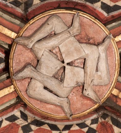 Zdjęcie nr 1: Rzeźbiony zwornik cylindryczny, z przedstawieniem sześciu wirujących, nagich nóg, ugiętych w kolanach, wychodzących promieniście z jednego punktu.