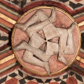 Zdjęcie nr 1: Rzeźbiony zwornik cylindryczny, z przedstawieniem sześciu wirujących, nagich nóg, ugiętych w kolanach, wychodzących promieniście z jednego punktu.