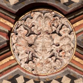 Zdjęcie nr 1: Rzeźbiony zwornik z przedstawieniem maski liściastej – twarzy ludzkiej wśród elementów roślinnych, liście wydobywają się z ust i przysłaniają policzki postaci.