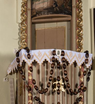 Zdjęcie nr 1: Ambona wisząca, przyścienna, z wejściem przez zaplecek od zakrystii. Kosz na planie prostokąta o wypukłej ścianie frontowej, na cokole w formie wałka, z podwieszeniem w kształcie ściętego ostrosłupa o wklęsłych bokach, zakończonego szyszką. Naroża kosza ujęte pilastrami z płycinami w trzonach, zdobionymi kampanulami, podtrzymującymi parapet w formie gzymsu. Ścianka frontowa dekorowana kanelurami, boczne prostokątnymi płycinami z rozetami. Zaplecek w formie stojącego prostokąta, ujęty listwami z cekinami oraz uszami utworzonymi z wijącego się ornamentu roślinnego. W polu drzwi, ponad którymi wypukła płaskorzeźba w formie leżącego prostokąta, z przedstawieniem siewcy na tle pejzażu. Baldachim na planie analogicznym względem kosza, z podwieszonymi lambrekinami, na nim cokół, na którym leży otwarta księga pośród obłoków, z dwiema uskrzydlonymi główkami anielskimi, w glorii promienistej. Nad nimi krzyż. Księga z napisem „LEX / ET / EVAN/GELIUM / I / II / III / IV / V / VI / VII / VIII / IX / X”. Na podniebieniu baldachimu gołębica Ducha Świętego. Z tyłu, na drzwiczkach widniał napis „I.K. 1831”. Struktura polichromowana w kolorze beżowym, jasnobrązowym i jasnoróżowym, ornamentyka złocona, detal srebrzony. 


