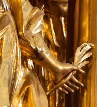 Zdjęcie nr 2: Rzeźba drążona, ustawiona na podstawie na planie kwadratu. Święta ukazana frontalnie, w kontrapoście, o esowato wygiętej sylwetce, z głową przechyloną na prawe ramię. Prawa ręka na piersi, w dłoni trzyma obcęgi zwieńczone lilią heraldyczną, lewa odchylona od boku, w dłoni ma liść palmy. Twarz ma owalną, o wydatnym podbródku, migdałowatych oczach, o głęboko rzeźbionych kącikach, prostym nosie i pełnych, rozchylonych ustach. Włosy ma długie, kręcone, sięgające ramion, zawinięte nad czołem. Ubrana jest w suknię przewiązaną w talii, z dekoltem odsłaniającym ramiona, ściśle przylegającą do ciała oraz w płaszcz zarzucony na lewe ramię i zawiązany z przodu postaci. Figura w całości złocona.