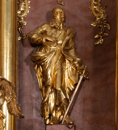 Zdjęcie nr 1: Rzeźba drążona, ustawiona na podstawie na plenie prostokąta. Święty ukazany frontalnie, z głową skierowaną w prawo, w kontrapoście, o delikatnie odchylonej w tył sylwetce. Prawą rękę kładzie na piersi, w lewej, odsuniętej od boku trzyma miecz skierowany ostrzem w dół. Twarz ma pociągłą, szczupłą, o wysokim czole, małych, migdałowatych oczach, prostym nosie i otwartych ustach, okoloną długą, kręconą brodą i krótkimi włosami, z pojedynczym puklem nad czołem i łysiną na głowie. Ubrany jest w tunikę przewiązaną pasem, ściśle przylegającą do ciała, z wywiniętymi mankietami oraz płaszcz zawieszony na lewym ramieniu, opadający na plecy, zawijający się na prawej nodze i zawiązany u pasa. Figura w całości złocona, ostrze miecza srebrzone.