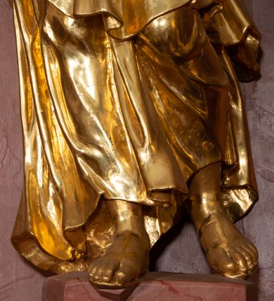 Zdjęcie nr 5: Rzeźba drążona, ustawiona na nieregularnej podstawie. Święty ukazany frontalnie, z głową skierowaną w lewo, w kontrapoście. Lewą rękę ma ugiętą i uniesioną w bok, w dłoni trzyma klucze, prawą ugiętą, przy boku, w której trzyma zamkniętą księgę. Twarz ma pociągłą, szczupłą, o małych, migdałowatych oczach, prostym nosie i pełnych, rozchylonych ustach, okoloną krótką, kręconą brodą i włosami. Ubrany jest w tunikę, rozchyloną na piersi, ściśle przylegająca do ciała, przepasaną w talii oraz obfity płaszcz zarzucony na prawe ramię i zawinięty na lewym boku i z przodu postaci. Figura w całości złocona.