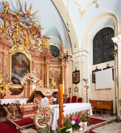 Zdjęcie nr 5: Nastawa ołtarzowa architektoniczna, jednokondygnacyjna ze zwieńczeniem, pięcioosiowa, ustawiona na wysokim cokole. Ołtarz wolnostojący, drewniany, sarkofagowy, wklęsło-wypukły, o zdwojonym froncie; mensa drewniana z marmurowym portatylem. Od frontu rocaille'owy kartusz ujęty fantazyjnymi płycinami oraz liśćmi. Na ołtarzu tabernakulum w formie sześcianu o wklęsłych bokach i wklęsło-wypukłym froncie; ujęte w narożach dwiema parami pilastrów o trzonach przechodzących w spływy wolutowe zdobione rocaille'm i różami. Pilastry podtrzymują falujący gzyms oraz fragmenty falistego, przerwanego, odwróconego przyczółka, przechodzącego w cokół, stanowiący tron wystawienia, na którym stoi krucyfiks. Na ściance frontowej obrotowa nisza, o wykroju stojącego prostokąta zamkniętego łukiem półkolistym, w opasce, zwieńczona kampanulami. W jej polu drzwiczki w formie stojącego prostokąta zamkniętego łukiem półkolistym w profilowanej ramie, z odlewanym przedstawieniem baranka leżącego na księdze z pieczęciami. Tabernakulum ujęte spływami przechodzącymi na krańcach we fragmenty wolutowego gzymsu, na których siedzą figury adorujących aniołów. Ponad tabernakulum fantazyjna ścianka tworząca tło dla tronu wystawienia z prześwitem otoczonym obłokami, z glorią promienistą, flankowana rocaille'owymi uszami. Cokół nastawy z wyodrębnionymi dwoma prostopadłościanami i dwoma konsolami, na dwóch skrajnych osiach bramki zamknięte wolutowymi szczytami tworzącymi cokoły dla figur, z przejściami w formie stojącego prostokąta zamkniętego łukiem odcinkowym nadwieszonym, z drzwiczkami. Cokół i drzwiczki dekorowane rocaille'm. Lico nastawy wklęsłe, osie wydzielone trzema parami pilastrów, na których tle stoją dwie pary kolumn o kapitelach kompozytowych. Podpory dźwigają pełne belkowanie, wyłamane na ich osi, przerwane nad polem środkowym, o gzymsie przechodzącym miejscami w rocaille'owe kartusze. Na osi środkowej wnęka z obrazem Matki Boskiej Wspomożenia Wiernych, w formie stojącego prostokąta zamkniętego łukiem odcinkowym nadwieszonym z uskokiem, ujęta profilowaną ramą, dekorowaną ponad łukiem płomienistym rocaille'm. Na pozostałych czterech osiach figury św. Barbary, św. Apolonii, św. Piotra i św. Pawła ustawione na rokokowych wspornikach. Trzony pilastrów i pola osi bocznych wypełnione rocaille'm, fryz dekorowany zwisami kwiatowymi. Zwieńczenie w formie zbliżonej do trapezu, zamknięte dwoma fragmentami gzymsu przechodzącego w woluty, flankowane wolutami spływającymi na belkowanie wewnętrznej pary kolumn, na których siedzą adorujące figury aniołów. W polu rzeźbiarska grupa Trójcy Świętej, pośród obłoków, w glorii promienistej, zwieńczona gołębicą Ducha Świętego w otoku z obłoków i uskrzydlonych główek anielskich, w glorii promienistej, flankowana przez dwa putta siedzące na gzymsie. Zwieńczenie po bokach obwiedzione rocaille'm, ujęte liśćmi palmowymi. Na belkowaniu, na osiach zewnętrznej pary kolumn wolutowe cokoły z rokokowymi wazonami. Struktura polichromowana na sposób imitujący marmoryzację w kolorze różowym i różowo-pomarańczowym, kolumny, profile i ornamentyka złocone, obłoki srebrzone. 

