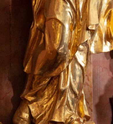 Zdjęcie nr 23: Nastawa ołtarzowa architektoniczna, jednokondygnacyjna ze zwieńczeniem, pięcioosiowa, ustawiona na wysokim cokole. Ołtarz wolnostojący, drewniany, sarkofagowy, wklęsło-wypukły, o zdwojonym froncie; mensa drewniana z marmurowym portatylem. Od frontu rocaille&#039;owy kartusz ujęty fantazyjnymi płycinami oraz liśćmi. Na ołtarzu tabernakulum w formie sześcianu o wklęsłych bokach i wklęsło-wypukłym froncie; ujęte w narożach dwiema parami pilastrów o trzonach przechodzących w spływy wolutowe zdobione rocaille&#039;m i różami. Pilastry podtrzymują falujący gzyms oraz fragmenty falistego, przerwanego, odwróconego przyczółka, przechodzącego w cokół, stanowiący tron wystawienia, na którym stoi krucyfiks. Na ściance frontowej obrotowa nisza, o wykroju stojącego prostokąta zamkniętego łukiem półkolistym, w opasce, zwieńczona kampanulami. W jej polu drzwiczki w formie stojącego prostokąta zamkniętego łukiem półkolistym w profilowanej ramie, z odlewanym przedstawieniem baranka leżącego na księdze z pieczęciami. Tabernakulum ujęte spływami przechodzącymi na krańcach we fragmenty wolutowego gzymsu, na których siedzą figury adorujących aniołów. Ponad tabernakulum fantazyjna ścianka tworząca tło dla tronu wystawienia z prześwitem otoczonym obłokami, z glorią promienistą, flankowana rocaille&#039;owymi uszami. Cokół nastawy z wyodrębnionymi dwoma prostopadłościanami i dwoma konsolami, na dwóch skrajnych osiach bramki zamknięte wolutowymi szczytami tworzącymi cokoły dla figur, z przejściami w formie stojącego prostokąta zamkniętego łukiem odcinkowym nadwieszonym, z drzwiczkami. Cokół i drzwiczki dekorowane rocaille&#039;m. Lico nastawy wklęsłe, osie wydzielone trzema parami pilastrów, na których tle stoją dwie pary kolumn o kapitelach kompozytowych. Podpory dźwigają pełne belkowanie, wyłamane na ich osi, przerwane nad polem środkowym, o gzymsie przechodzącym miejscami w rocaille&#039;owe kartusze. Na osi środkowej wnęka z obrazem Matki Boskiej Wspomożenia Wiernych, w formie stojącego prostokąta zamkniętego łukiem odcinkowym nadwieszonym z uskokiem, ujęta profilowaną ramą, dekorowaną ponad łukiem płomienistym rocaille&#039;m. Na pozostałych czterech osiach figury św. Barbary, św. Apolonii, św. Piotra i św. Pawła ustawione na rokokowych wspornikach. Trzony pilastrów i pola osi bocznych wypełnione rocaille&#039;m, fryz dekorowany zwisami kwiatowymi. Zwieńczenie w formie zbliżonej do trapezu, zamknięte dwoma fragmentami gzymsu przechodzącego w woluty, flankowane wolutami spływającymi na belkowanie wewnętrznej pary kolumn, na których siedzą adorujące figury aniołów. W polu rzeźbiarska grupa Trójcy Świętej, pośród obłoków, w glorii promienistej, zwieńczona gołębicą Ducha Świętego w otoku z obłoków i uskrzydlonych główek anielskich, w glorii promienistej, flankowana przez dwa putta siedzące na gzymsie. Zwieńczenie po bokach obwiedzione rocaille&#039;m, ujęte liśćmi palmowymi. Na belkowaniu, na osiach zewnętrznej pary kolumn wolutowe cokoły z rokokowymi wazonami. Struktura polichromowana na sposób imitujący marmoryzację w kolorze różowym i różowo-pomarańczowym, kolumny, profile i ornamentyka złocone, obłoki srebrzone. 

