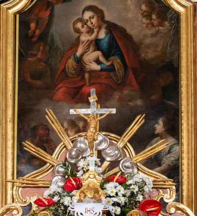 Zdjęcie nr 28: Nastawa ołtarzowa architektoniczna, jednokondygnacyjna ze zwieńczeniem, pięcioosiowa, ustawiona na wysokim cokole. Ołtarz wolnostojący, drewniany, sarkofagowy, wklęsło-wypukły, o zdwojonym froncie; mensa drewniana z marmurowym portatylem. Od frontu rocaille&#039;owy kartusz ujęty fantazyjnymi płycinami oraz liśćmi. Na ołtarzu tabernakulum w formie sześcianu o wklęsłych bokach i wklęsło-wypukłym froncie; ujęte w narożach dwiema parami pilastrów o trzonach przechodzących w spływy wolutowe zdobione rocaille&#039;m i różami. Pilastry podtrzymują falujący gzyms oraz fragmenty falistego, przerwanego, odwróconego przyczółka, przechodzącego w cokół, stanowiący tron wystawienia, na którym stoi krucyfiks. Na ściance frontowej obrotowa nisza, o wykroju stojącego prostokąta zamkniętego łukiem półkolistym, w opasce, zwieńczona kampanulami. W jej polu drzwiczki w formie stojącego prostokąta zamkniętego łukiem półkolistym w profilowanej ramie, z odlewanym przedstawieniem baranka leżącego na księdze z pieczęciami. Tabernakulum ujęte spływami przechodzącymi na krańcach we fragmenty wolutowego gzymsu, na których siedzą figury adorujących aniołów. Ponad tabernakulum fantazyjna ścianka tworząca tło dla tronu wystawienia z prześwitem otoczonym obłokami, z glorią promienistą, flankowana rocaille&#039;owymi uszami. Cokół nastawy z wyodrębnionymi dwoma prostopadłościanami i dwoma konsolami, na dwóch skrajnych osiach bramki zamknięte wolutowymi szczytami tworzącymi cokoły dla figur, z przejściami w formie stojącego prostokąta zamkniętego łukiem odcinkowym nadwieszonym, z drzwiczkami. Cokół i drzwiczki dekorowane rocaille&#039;m. Lico nastawy wklęsłe, osie wydzielone trzema parami pilastrów, na których tle stoją dwie pary kolumn o kapitelach kompozytowych. Podpory dźwigają pełne belkowanie, wyłamane na ich osi, przerwane nad polem środkowym, o gzymsie przechodzącym miejscami w rocaille&#039;owe kartusze. Na osi środkowej wnęka z obrazem Matki Boskiej Wspomożenia Wiernych, w formie stojącego prostokąta zamkniętego łukiem odcinkowym nadwieszonym z uskokiem, ujęta profilowaną ramą, dekorowaną ponad łukiem płomienistym rocaille&#039;m. Na pozostałych czterech osiach figury św. Barbary, św. Apolonii, św. Piotra i św. Pawła ustawione na rokokowych wspornikach. Trzony pilastrów i pola osi bocznych wypełnione rocaille&#039;m, fryz dekorowany zwisami kwiatowymi. Zwieńczenie w formie zbliżonej do trapezu, zamknięte dwoma fragmentami gzymsu przechodzącego w woluty, flankowane wolutami spływającymi na belkowanie wewnętrznej pary kolumn, na których siedzą adorujące figury aniołów. W polu rzeźbiarska grupa Trójcy Świętej, pośród obłoków, w glorii promienistej, zwieńczona gołębicą Ducha Świętego w otoku z obłoków i uskrzydlonych główek anielskich, w glorii promienistej, flankowana przez dwa putta siedzące na gzymsie. Zwieńczenie po bokach obwiedzione rocaille&#039;m, ujęte liśćmi palmowymi. Na belkowaniu, na osiach zewnętrznej pary kolumn wolutowe cokoły z rokokowymi wazonami. Struktura polichromowana na sposób imitujący marmoryzację w kolorze różowym i różowo-pomarańczowym, kolumny, profile i ornamentyka złocone, obłoki srebrzone. 

