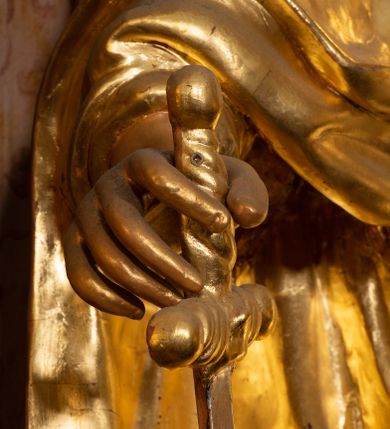 Zdjęcie nr 29: Nastawa ołtarzowa architektoniczna, jednokondygnacyjna ze zwieńczeniem, pięcioosiowa, ustawiona na wysokim cokole. Ołtarz wolnostojący, drewniany, sarkofagowy, wklęsło-wypukły, o zdwojonym froncie; mensa drewniana z marmurowym portatylem. Od frontu rocaille'owy kartusz ujęty fantazyjnymi płycinami oraz liśćmi. Na ołtarzu tabernakulum w formie sześcianu o wklęsłych bokach i wklęsło-wypukłym froncie; ujęte w narożach dwiema parami pilastrów o trzonach przechodzących w spływy wolutowe zdobione rocaille'm i różami. Pilastry podtrzymują falujący gzyms oraz fragmenty falistego, przerwanego, odwróconego przyczółka, przechodzącego w cokół, stanowiący tron wystawienia, na którym stoi krucyfiks. Na ściance frontowej obrotowa nisza, o wykroju stojącego prostokąta zamkniętego łukiem półkolistym, w opasce, zwieńczona kampanulami. W jej polu drzwiczki w formie stojącego prostokąta zamkniętego łukiem półkolistym w profilowanej ramie, z odlewanym przedstawieniem baranka leżącego na księdze z pieczęciami. Tabernakulum ujęte spływami przechodzącymi na krańcach we fragmenty wolutowego gzymsu, na których siedzą figury adorujących aniołów. Ponad tabernakulum fantazyjna ścianka tworząca tło dla tronu wystawienia z prześwitem otoczonym obłokami, z glorią promienistą, flankowana rocaille'owymi uszami. Cokół nastawy z wyodrębnionymi dwoma prostopadłościanami i dwoma konsolami, na dwóch skrajnych osiach bramki zamknięte wolutowymi szczytami tworzącymi cokoły dla figur, z przejściami w formie stojącego prostokąta zamkniętego łukiem odcinkowym nadwieszonym, z drzwiczkami. Cokół i drzwiczki dekorowane rocaille'm. Lico nastawy wklęsłe, osie wydzielone trzema parami pilastrów, na których tle stoją dwie pary kolumn o kapitelach kompozytowych. Podpory dźwigają pełne belkowanie, wyłamane na ich osi, przerwane nad polem środkowym, o gzymsie przechodzącym miejscami w rocaille'owe kartusze. Na osi środkowej wnęka z obrazem Matki Boskiej Wspomożenia Wiernych, w formie stojącego prostokąta zamkniętego łukiem odcinkowym nadwieszonym z uskokiem, ujęta profilowaną ramą, dekorowaną ponad łukiem płomienistym rocaille'm. Na pozostałych czterech osiach figury św. Barbary, św. Apolonii, św. Piotra i św. Pawła ustawione na rokokowych wspornikach. Trzony pilastrów i pola osi bocznych wypełnione rocaille'm, fryz dekorowany zwisami kwiatowymi. Zwieńczenie w formie zbliżonej do trapezu, zamknięte dwoma fragmentami gzymsu przechodzącego w woluty, flankowane wolutami spływającymi na belkowanie wewnętrznej pary kolumn, na których siedzą adorujące figury aniołów. W polu rzeźbiarska grupa Trójcy Świętej, pośród obłoków, w glorii promienistej, zwieńczona gołębicą Ducha Świętego w otoku z obłoków i uskrzydlonych główek anielskich, w glorii promienistej, flankowana przez dwa putta siedzące na gzymsie. Zwieńczenie po bokach obwiedzione rocaille'm, ujęte liśćmi palmowymi. Na belkowaniu, na osiach zewnętrznej pary kolumn wolutowe cokoły z rokokowymi wazonami. Struktura polichromowana na sposób imitujący marmoryzację w kolorze różowym i różowo-pomarańczowym, kolumny, profile i ornamentyka złocone, obłoki srebrzone. 

