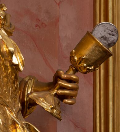 Zdjęcie nr 31: Nastawa ołtarzowa architektoniczna, jednokondygnacyjna ze zwieńczeniem, pięcioosiowa, ustawiona na wysokim cokole. Ołtarz wolnostojący, drewniany, sarkofagowy, wklęsło-wypukły, o zdwojonym froncie; mensa drewniana z marmurowym portatylem. Od frontu rocaille'owy kartusz ujęty fantazyjnymi płycinami oraz liśćmi. Na ołtarzu tabernakulum w formie sześcianu o wklęsłych bokach i wklęsło-wypukłym froncie; ujęte w narożach dwiema parami pilastrów o trzonach przechodzących w spływy wolutowe zdobione rocaille'm i różami. Pilastry podtrzymują falujący gzyms oraz fragmenty falistego, przerwanego, odwróconego przyczółka, przechodzącego w cokół, stanowiący tron wystawienia, na którym stoi krucyfiks. Na ściance frontowej obrotowa nisza, o wykroju stojącego prostokąta zamkniętego łukiem półkolistym, w opasce, zwieńczona kampanulami. W jej polu drzwiczki w formie stojącego prostokąta zamkniętego łukiem półkolistym w profilowanej ramie, z odlewanym przedstawieniem baranka leżącego na księdze z pieczęciami. Tabernakulum ujęte spływami przechodzącymi na krańcach we fragmenty wolutowego gzymsu, na których siedzą figury adorujących aniołów. Ponad tabernakulum fantazyjna ścianka tworząca tło dla tronu wystawienia z prześwitem otoczonym obłokami, z glorią promienistą, flankowana rocaille'owymi uszami. Cokół nastawy z wyodrębnionymi dwoma prostopadłościanami i dwoma konsolami, na dwóch skrajnych osiach bramki zamknięte wolutowymi szczytami tworzącymi cokoły dla figur, z przejściami w formie stojącego prostokąta zamkniętego łukiem odcinkowym nadwieszonym, z drzwiczkami. Cokół i drzwiczki dekorowane rocaille'm. Lico nastawy wklęsłe, osie wydzielone trzema parami pilastrów, na których tle stoją dwie pary kolumn o kapitelach kompozytowych. Podpory dźwigają pełne belkowanie, wyłamane na ich osi, przerwane nad polem środkowym, o gzymsie przechodzącym miejscami w rocaille'owe kartusze. Na osi środkowej wnęka z obrazem Matki Boskiej Wspomożenia Wiernych, w formie stojącego prostokąta zamkniętego łukiem odcinkowym nadwieszonym z uskokiem, ujęta profilowaną ramą, dekorowaną ponad łukiem płomienistym rocaille'm. Na pozostałych czterech osiach figury św. Barbary, św. Apolonii, św. Piotra i św. Pawła ustawione na rokokowych wspornikach. Trzony pilastrów i pola osi bocznych wypełnione rocaille'm, fryz dekorowany zwisami kwiatowymi. Zwieńczenie w formie zbliżonej do trapezu, zamknięte dwoma fragmentami gzymsu przechodzącego w woluty, flankowane wolutami spływającymi na belkowanie wewnętrznej pary kolumn, na których siedzą adorujące figury aniołów. W polu rzeźbiarska grupa Trójcy Świętej, pośród obłoków, w glorii promienistej, zwieńczona gołębicą Ducha Świętego w otoku z obłoków i uskrzydlonych główek anielskich, w glorii promienistej, flankowana przez dwa putta siedzące na gzymsie. Zwieńczenie po bokach obwiedzione rocaille'm, ujęte liśćmi palmowymi. Na belkowaniu, na osiach zewnętrznej pary kolumn wolutowe cokoły z rokokowymi wazonami. Struktura polichromowana na sposób imitujący marmoryzację w kolorze różowym i różowo-pomarańczowym, kolumny, profile i ornamentyka złocone, obłoki srebrzone. 

